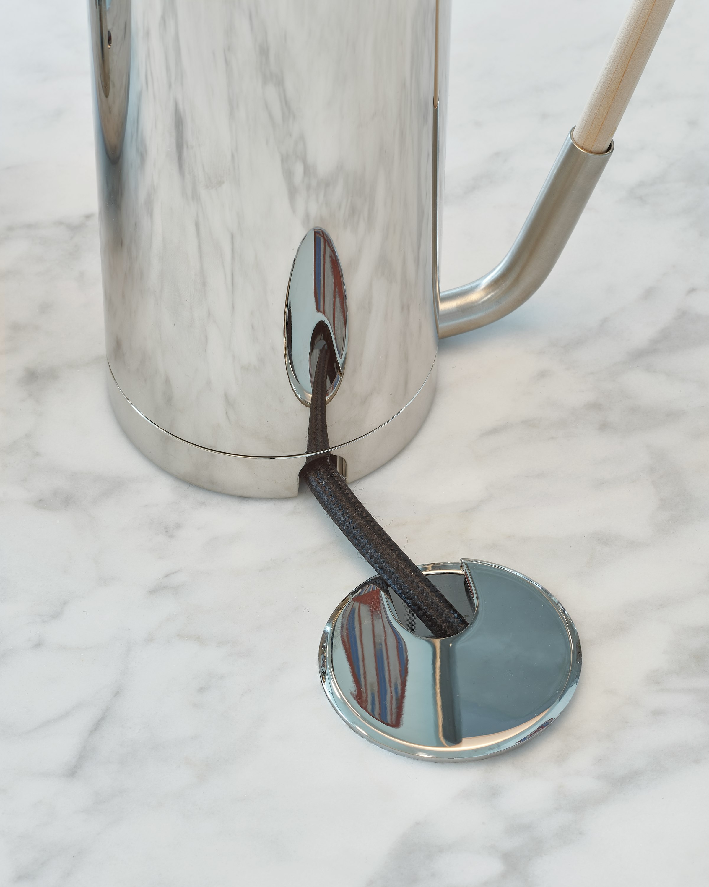 Detail view of a Parsons Table tabletop in White Carrara Marble with a chrome grommet, displaying cable management capabilities, viewed from above at an angle.