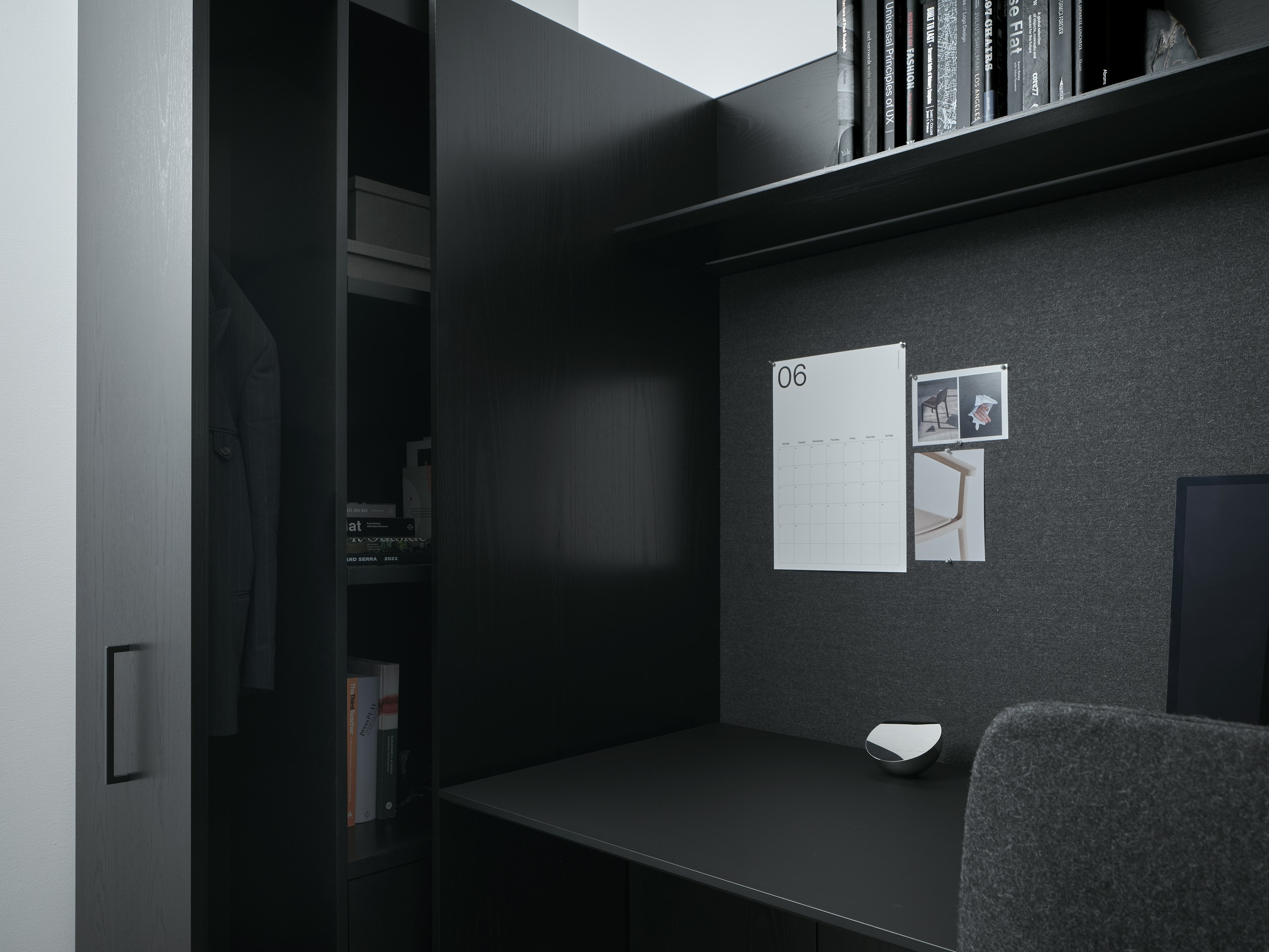 Detail view of a Geiger One Private Office in Ebonized Flat Cut Ash with an open wardrobe, overhead shelf, and a soft-touch laminate work surface, viewed at an angle.