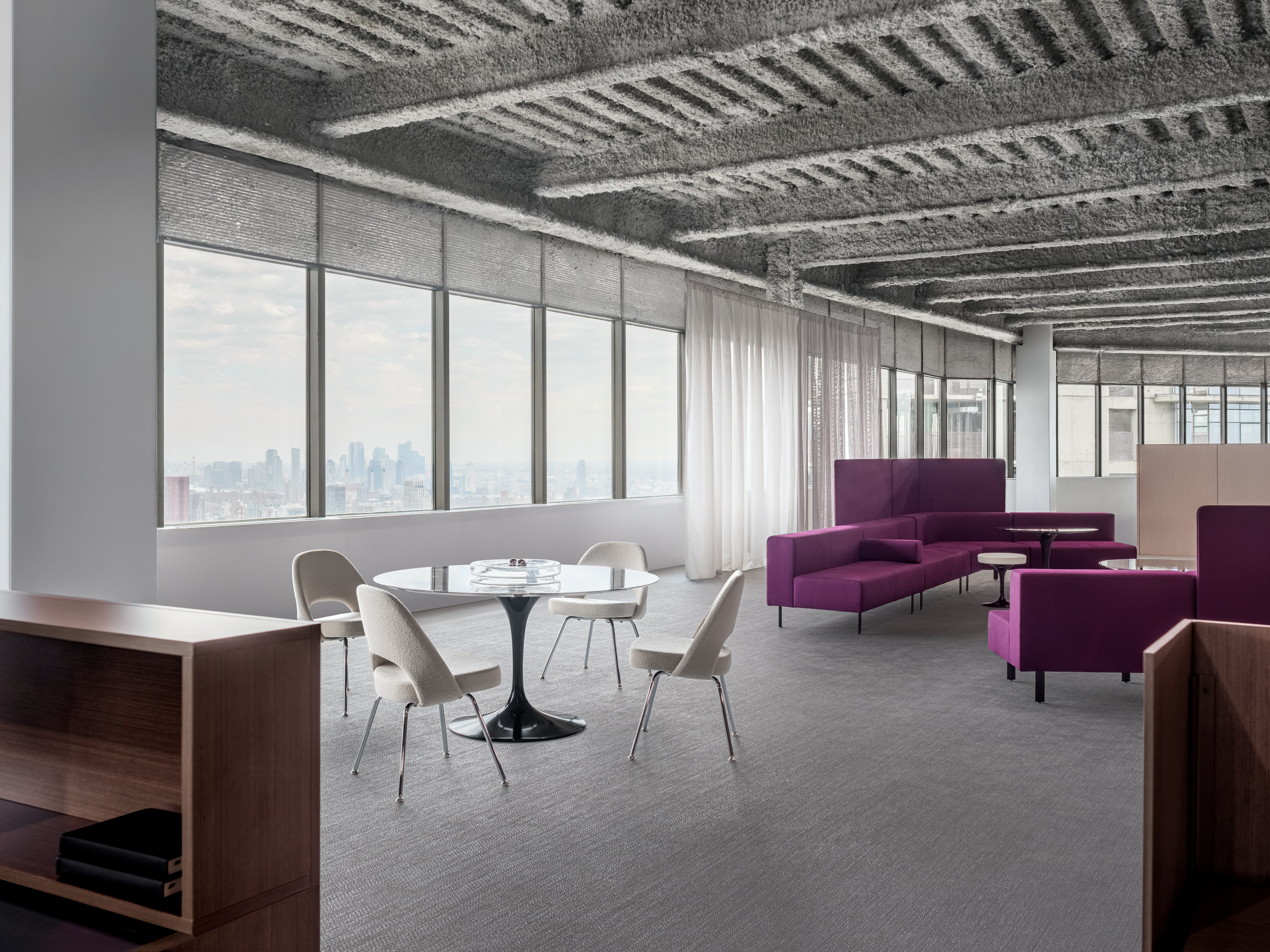 A open office floor plan has several settings, including a small meeting table with four chairs and lounge bench seating.