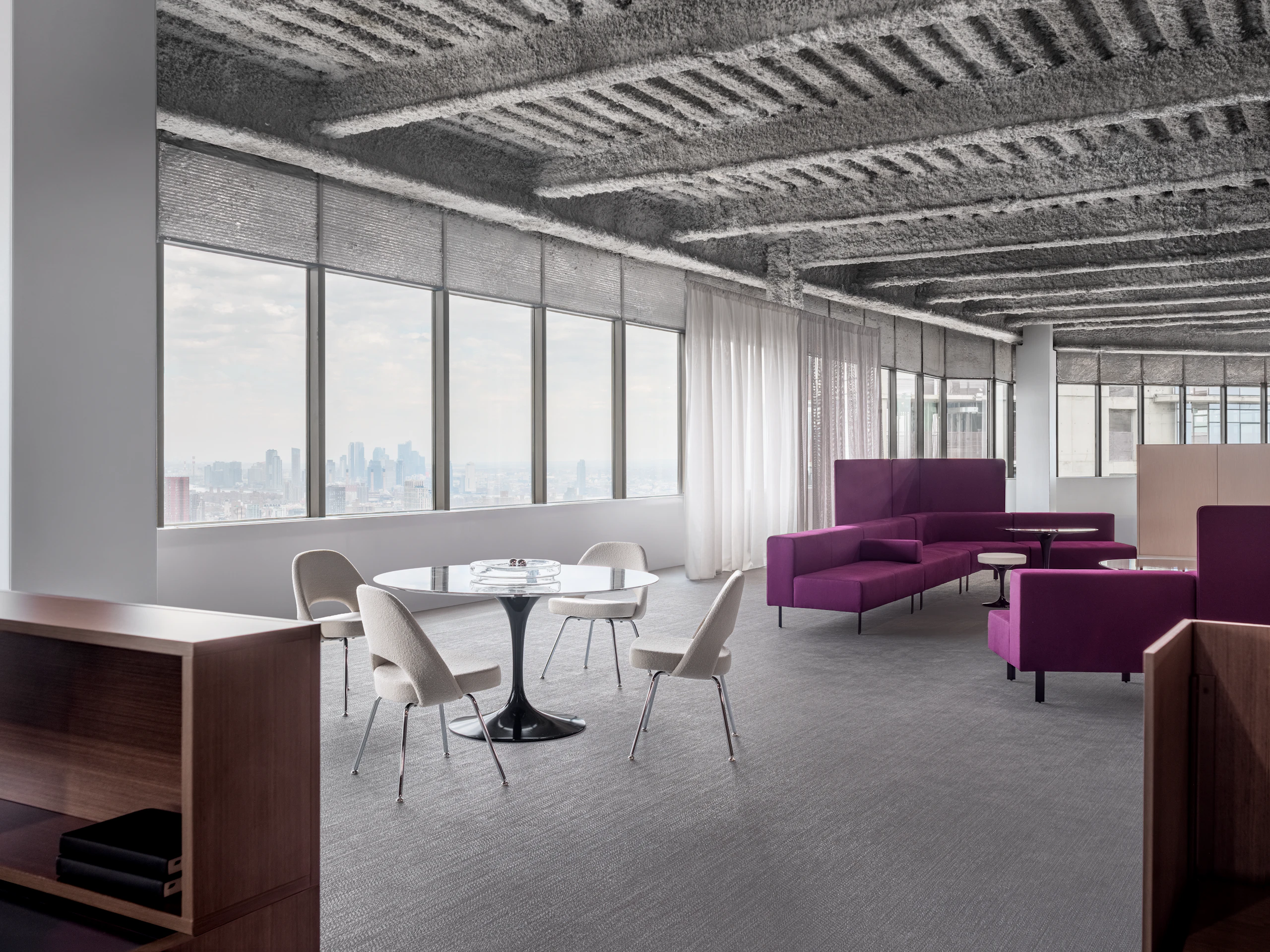 A open office floor plan has several settings, including a small meeting table with four chairs and lounge bench seating.