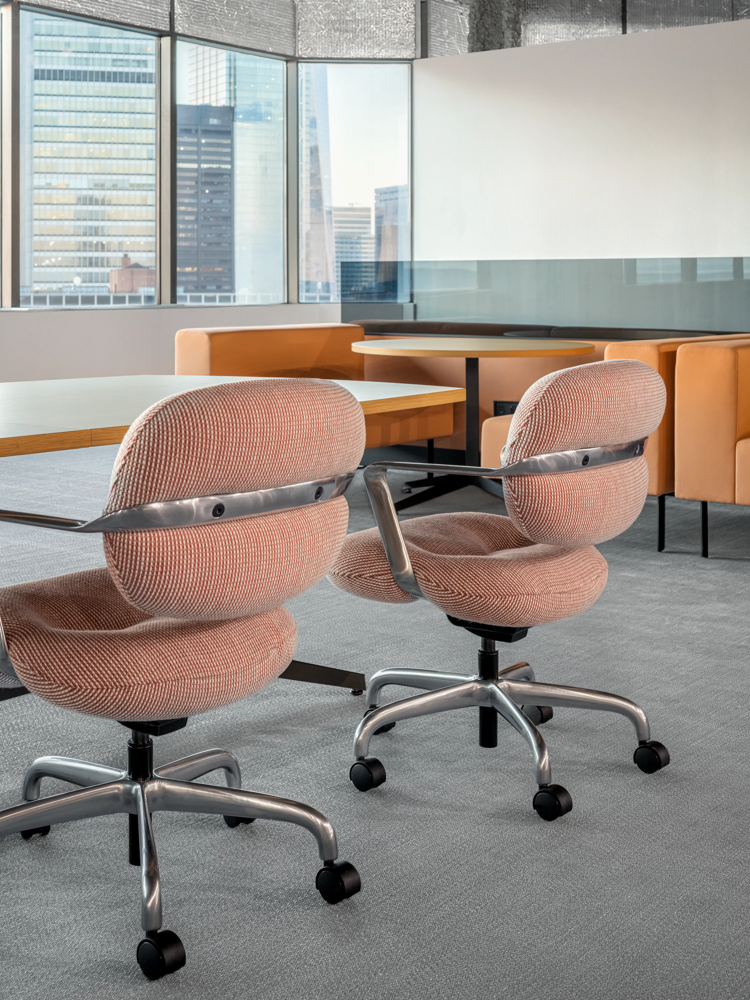 A meeting table with chairs is viewed at an angle with some casual lounge booths with tables is in the background.