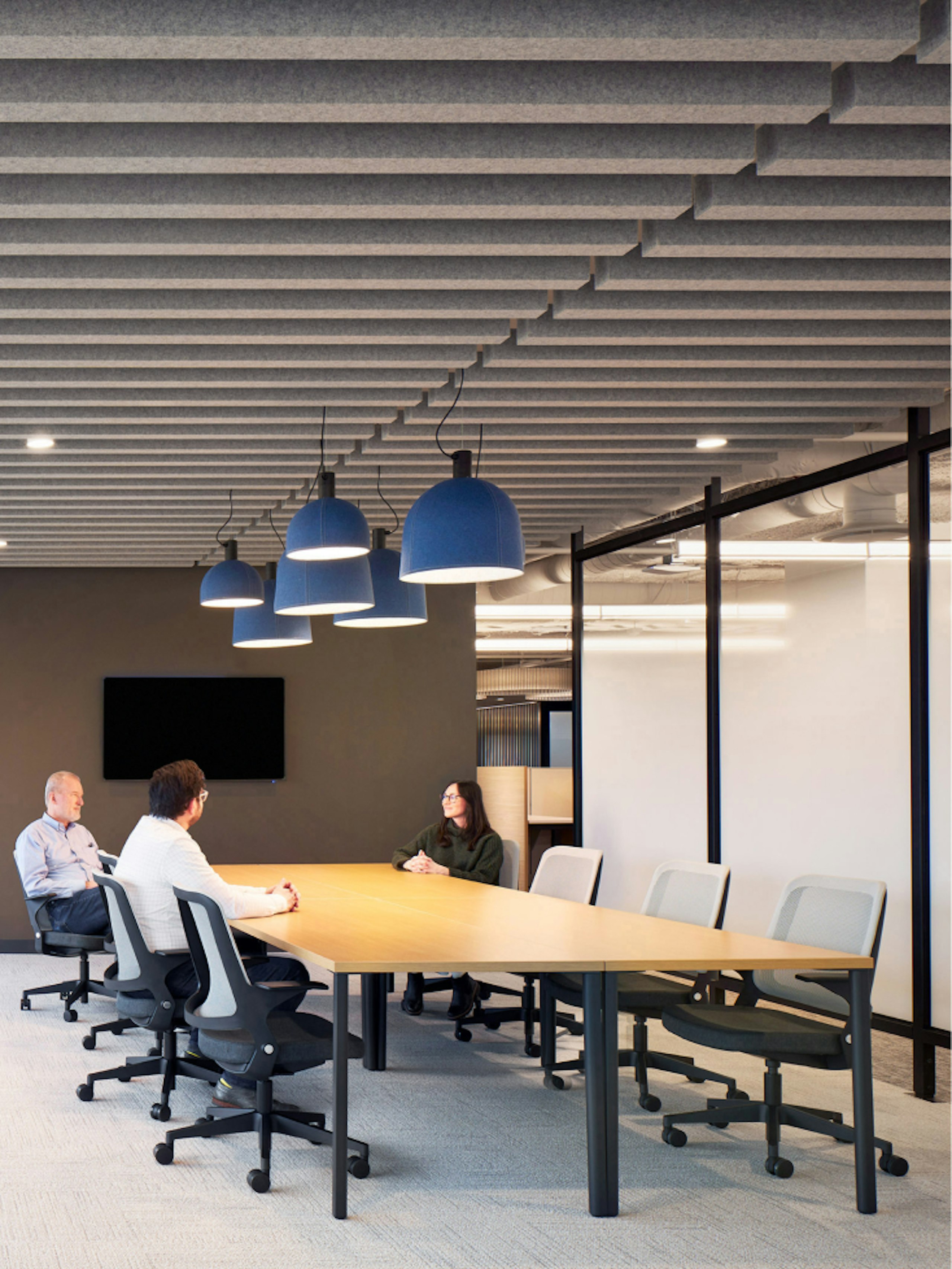 Three people sitting in black and white Knoll Ollo chairs while conversing at a large conference room table