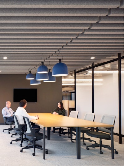 Three people sitting in black and white Knoll Ollo chairs while conversing at a large conference room table
