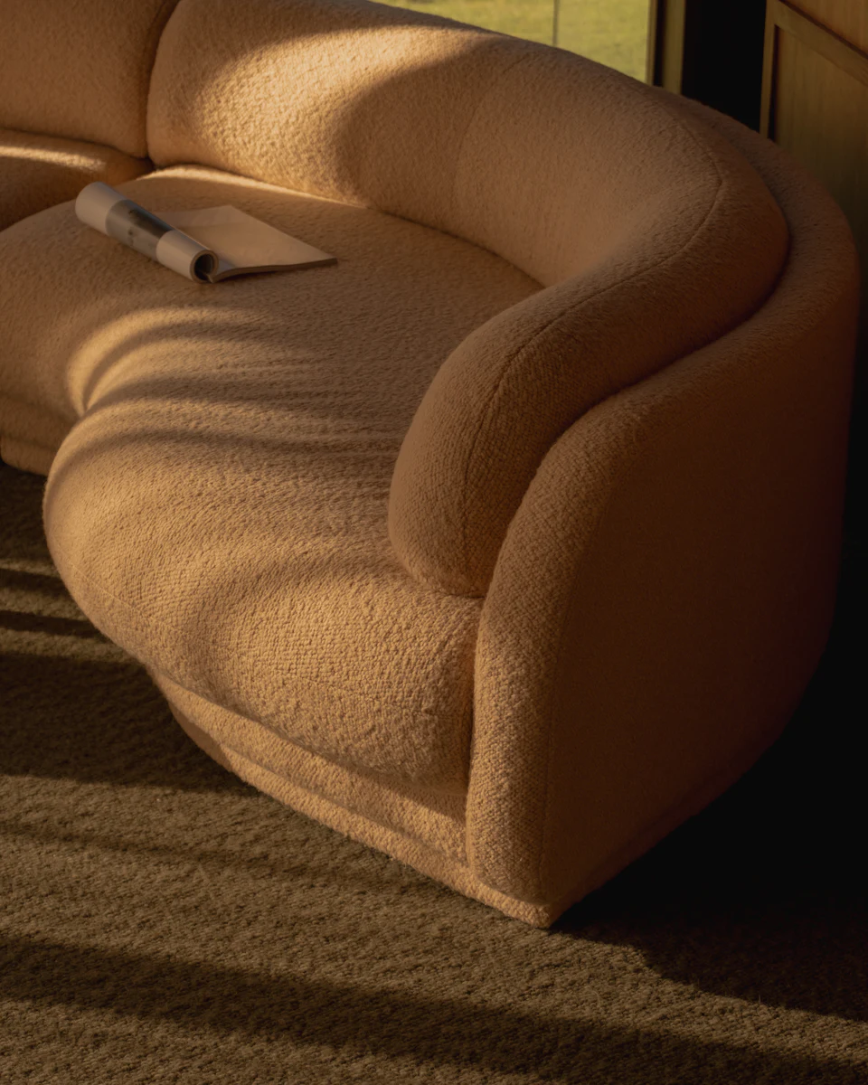 Beige curved sectional sofa with matching upholstery in corner of room
