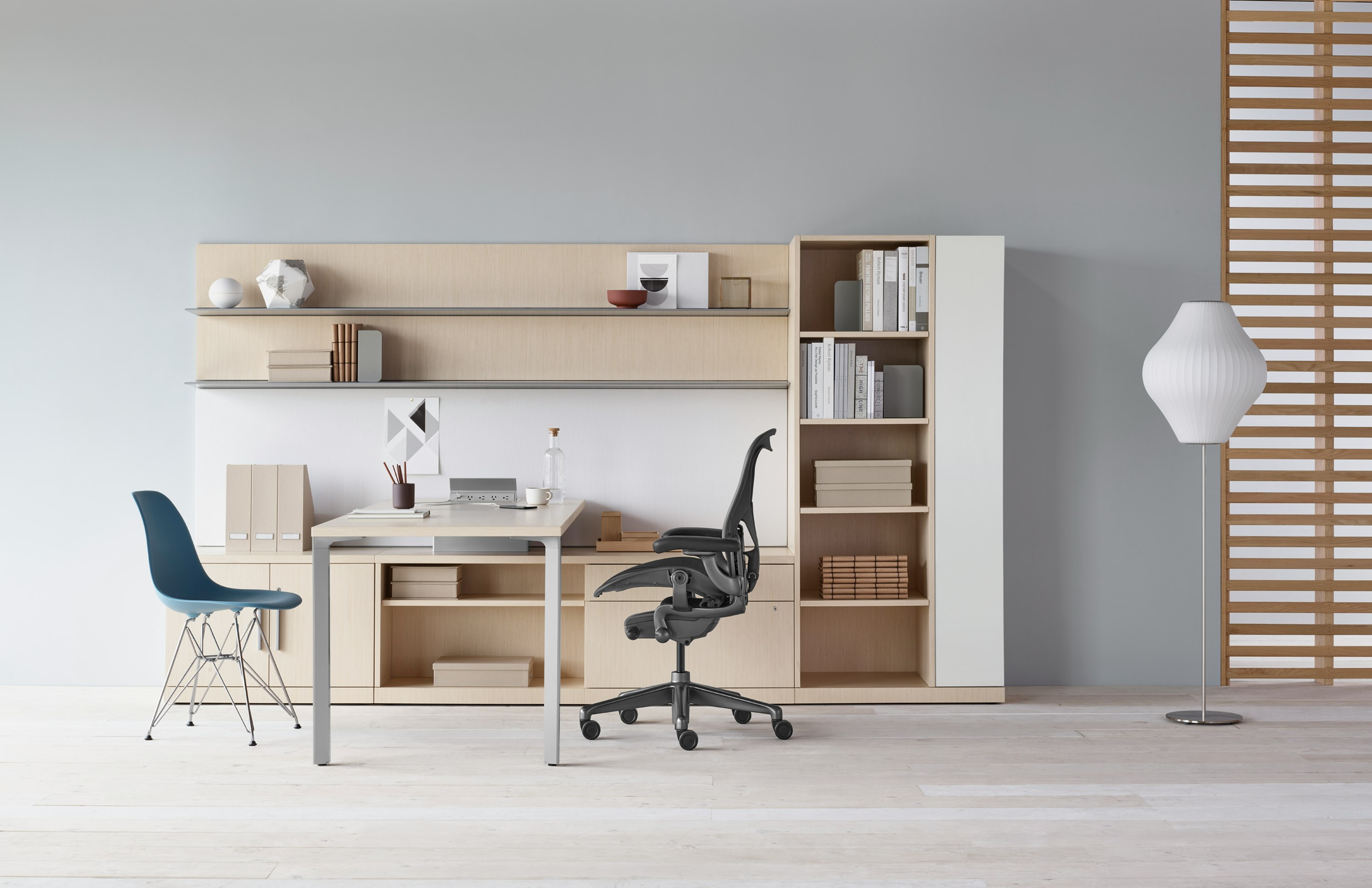 A Canvas Private Office with light wood storage, upper shelves, black Aeron chair, and blue Eames Molded Plastic side chair.