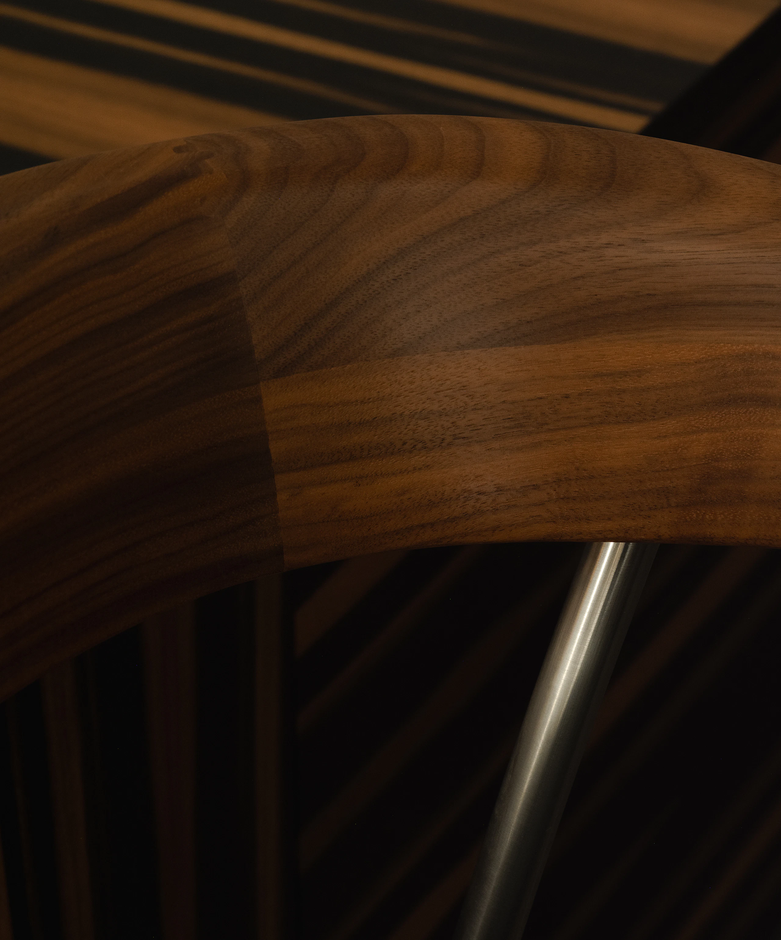 Detail view of a Leeway Stool backrest in Natural Walnut with a satin chrome frame, viewed at an angle.