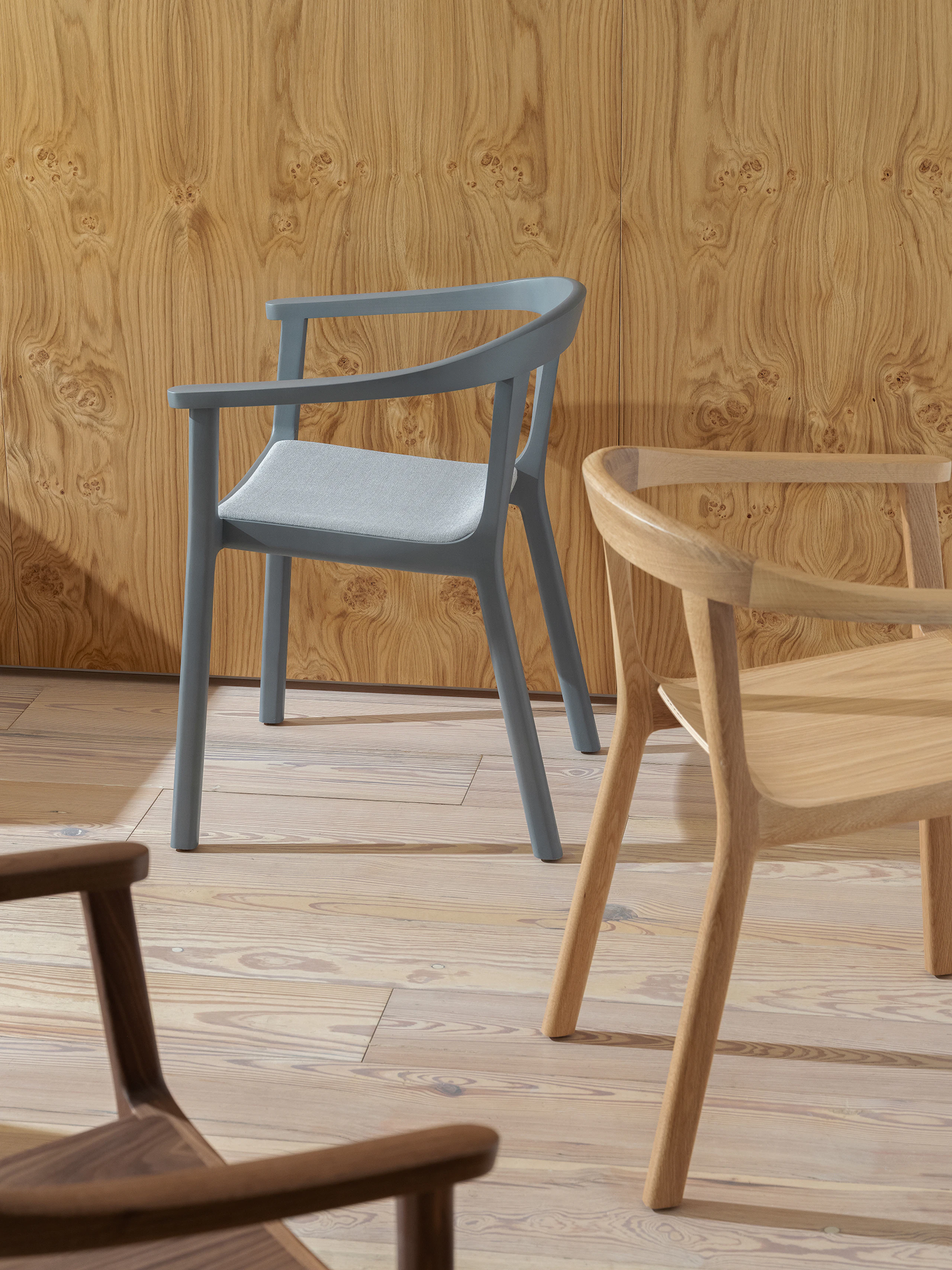 Three Lijn Armchairs designed by Carole Baijings in Natural Walnut, Natural Oak, and Nordic Blue, shown at varying angles, against a veneer wall.