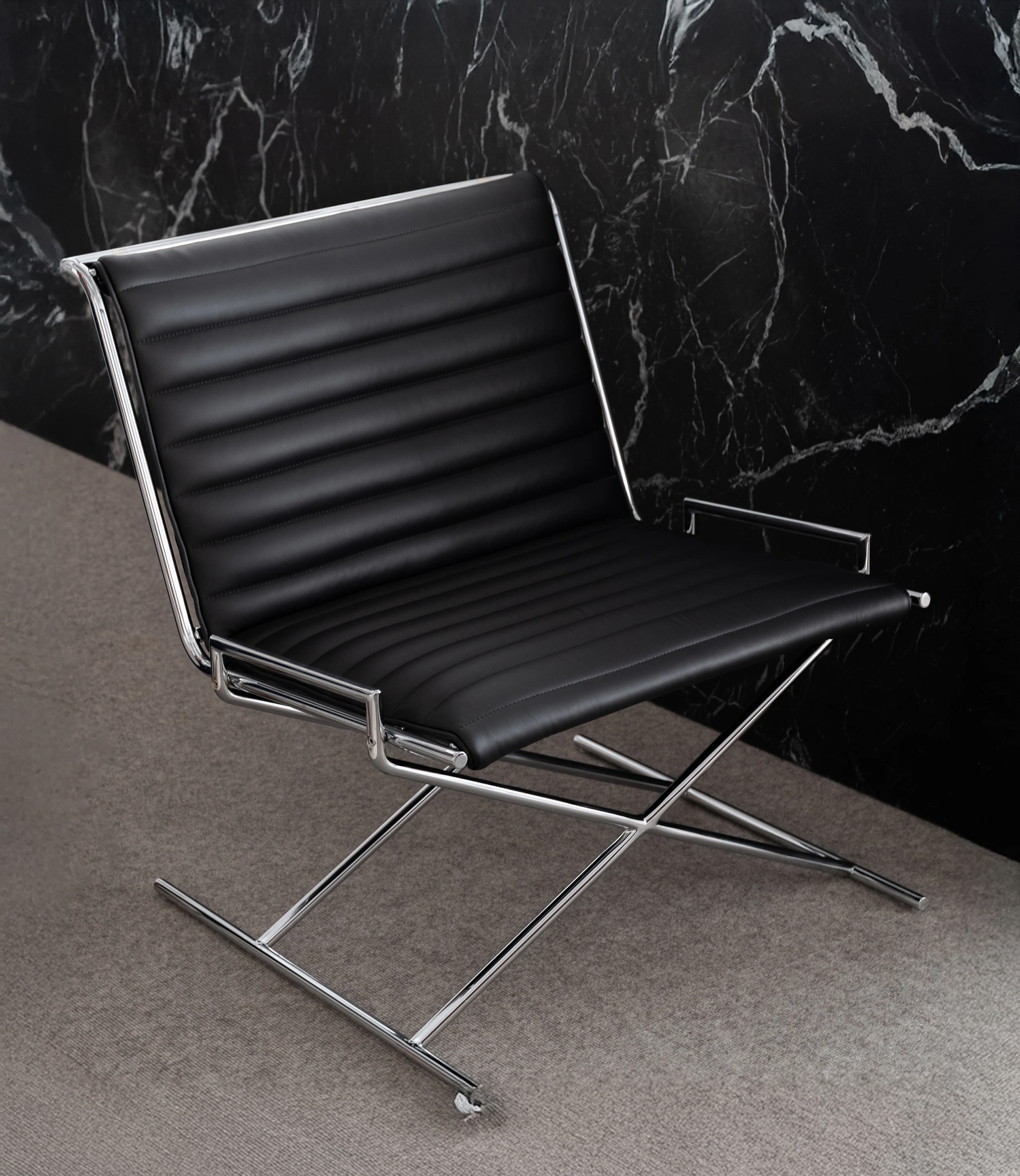 Sled Chair designed by Ward Bennett upholstered with black leather with a chrome frame, viewed against a black marble wall at an angle.