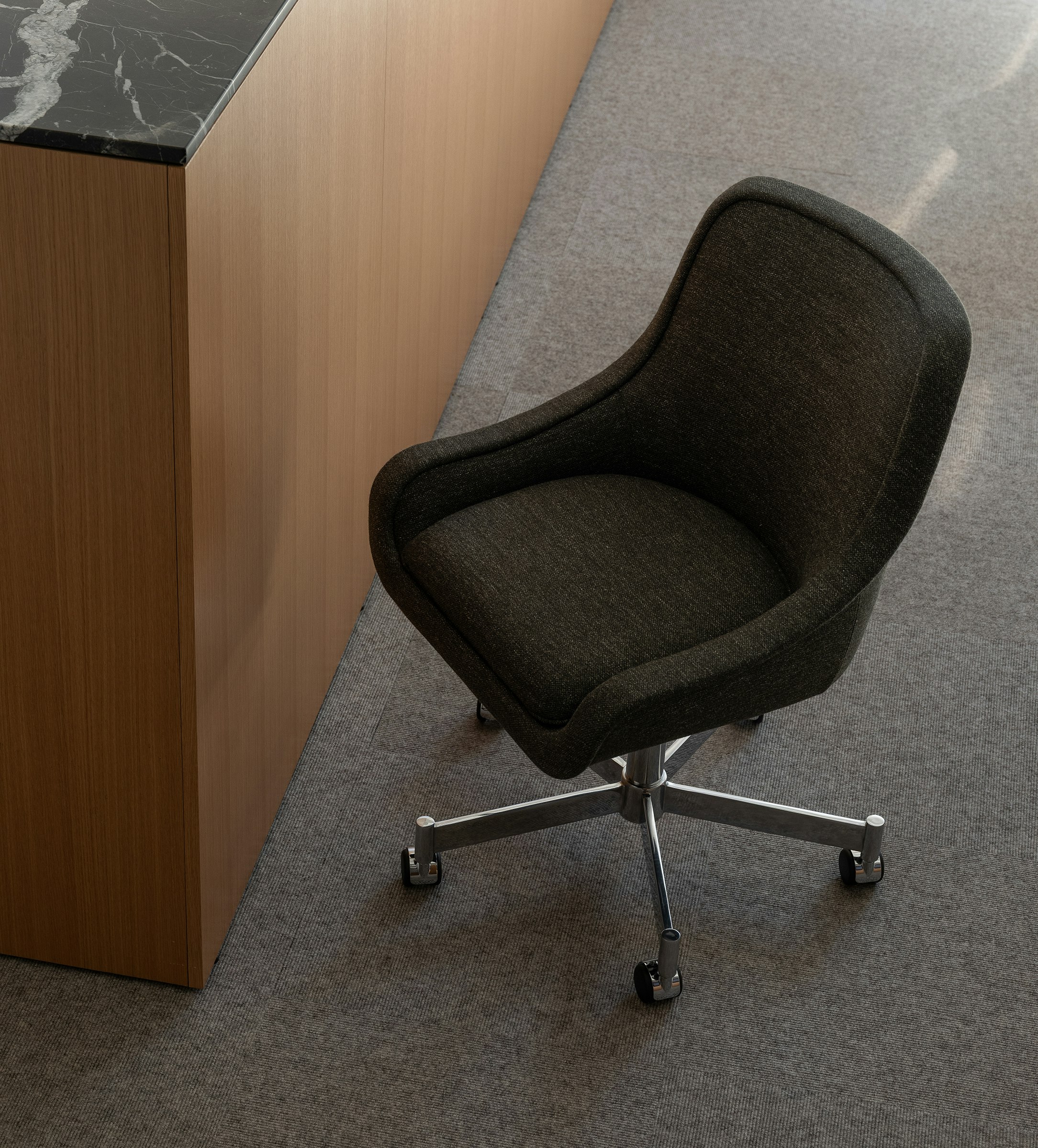 Bumper Conference Chair with low arms designed by Ward Bennett upholstered with Bellano in Black Green in a showroom setting, viewed from above at an angle