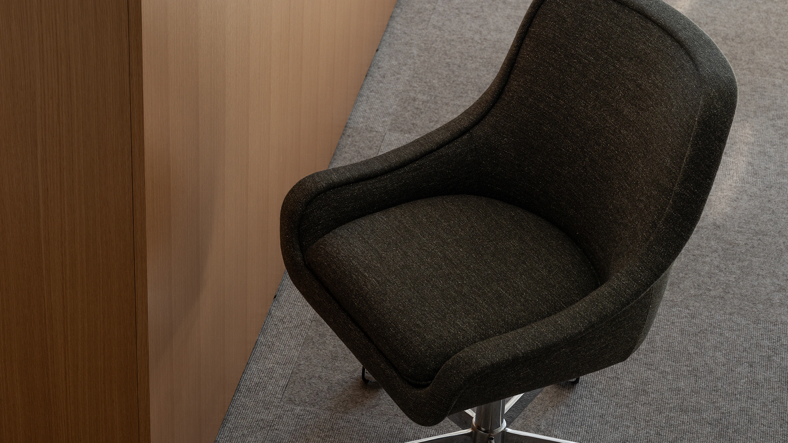 Bumper Conference Chair with low arms designed by Ward Bennett upholstered with Bellano in Black Green in a showroom setting, viewed from above at an angle