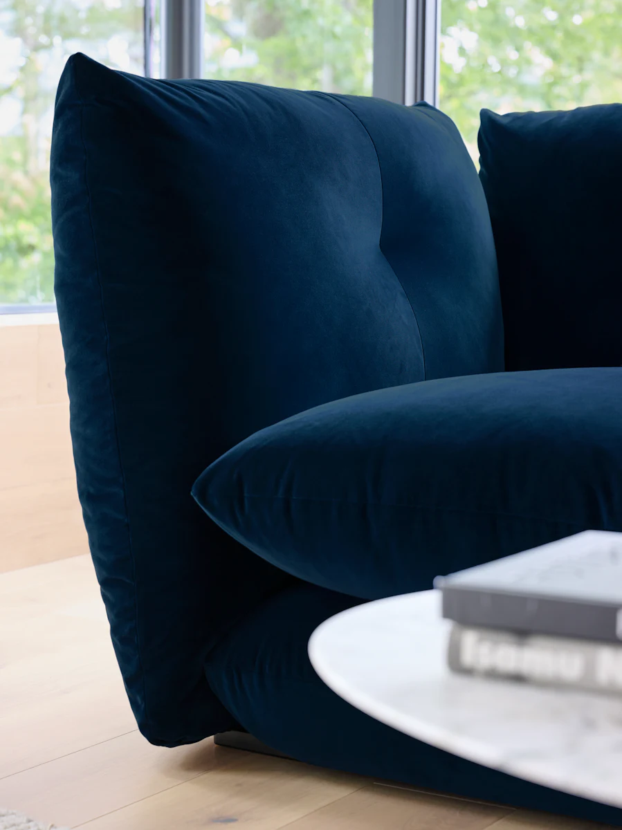 Dark blue upholstered sofa with rounded cushions and near round white coffee table