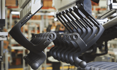 Several pieces of plastic pieces used in furniture manufacturing hanging from a rack on an assembly line..