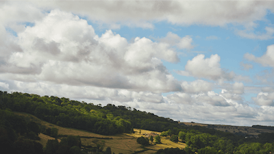 Green, rolling hills blanketed in trees beneath a cloudy sky.