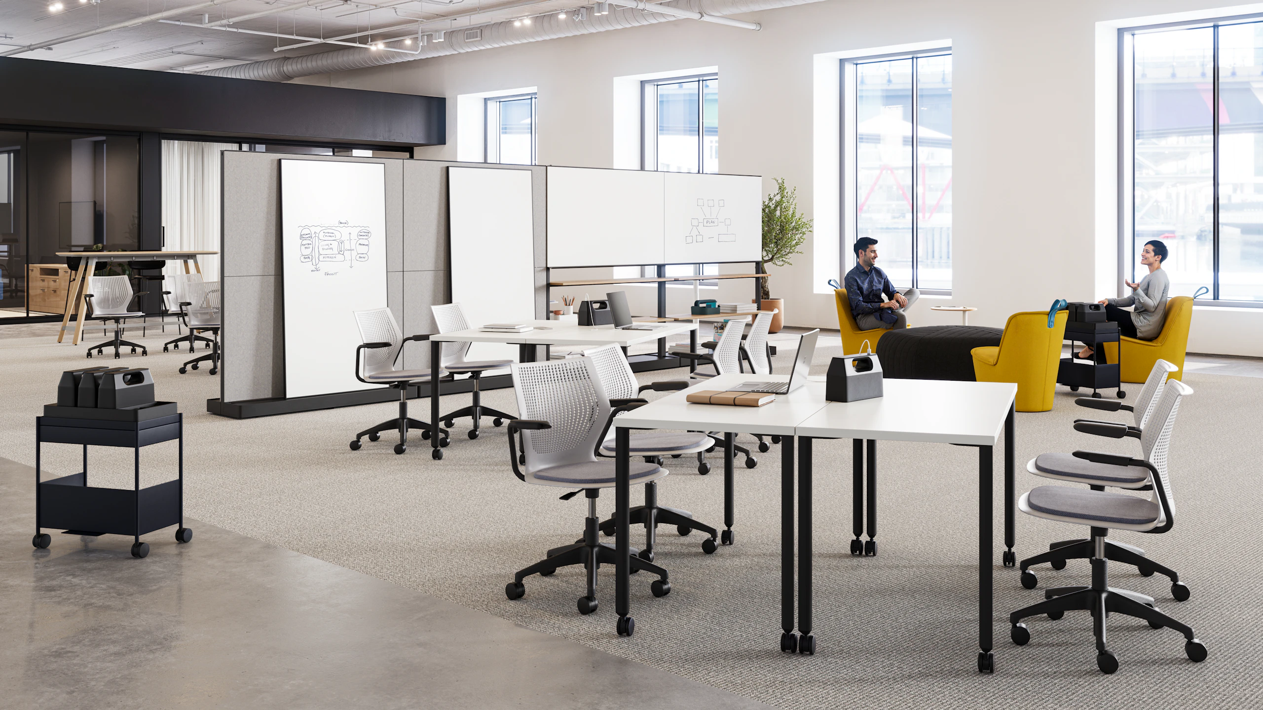 Two people sitting in a brightly lit, open floorplan community setting featuring Herman Miller Fuld Nesting chairs, yellow NaughtOne Pippin chairs, and Herman Miller OE1 Agile Walls and Storage Trolleys.