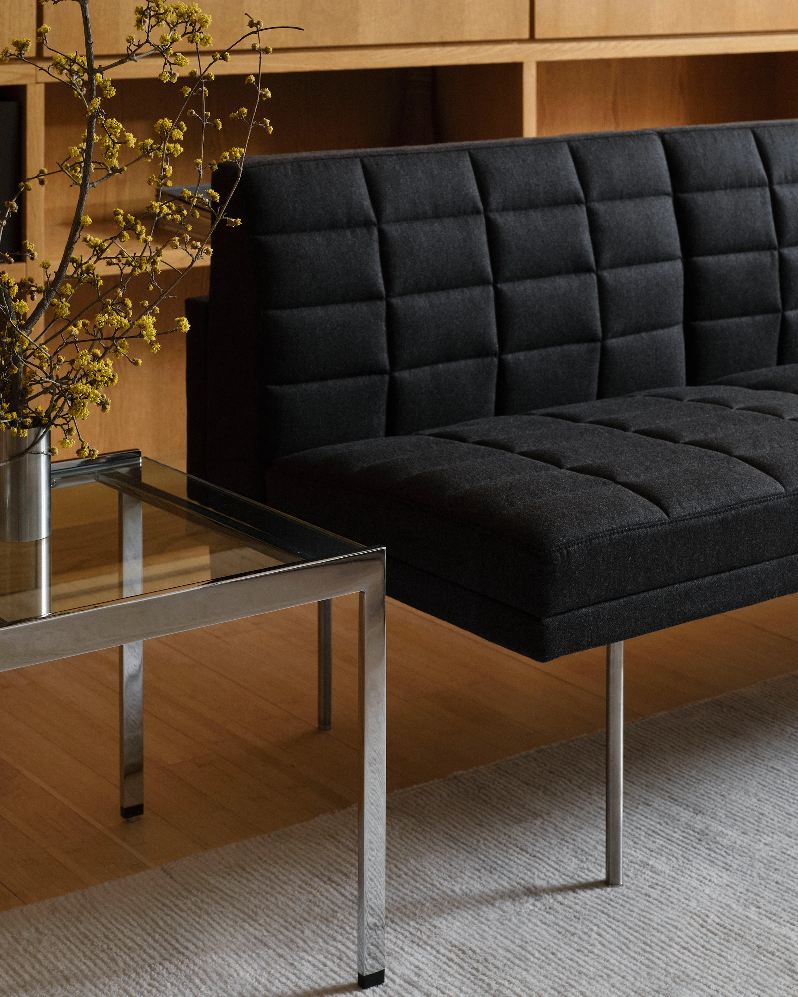 Partial view of a Tuxedo Component Sofa upholstered with Bellano in Black Green beside an H Frame Coffee Table with a clear glass top and chrome frame, viewed at an angle in a lounge setting.