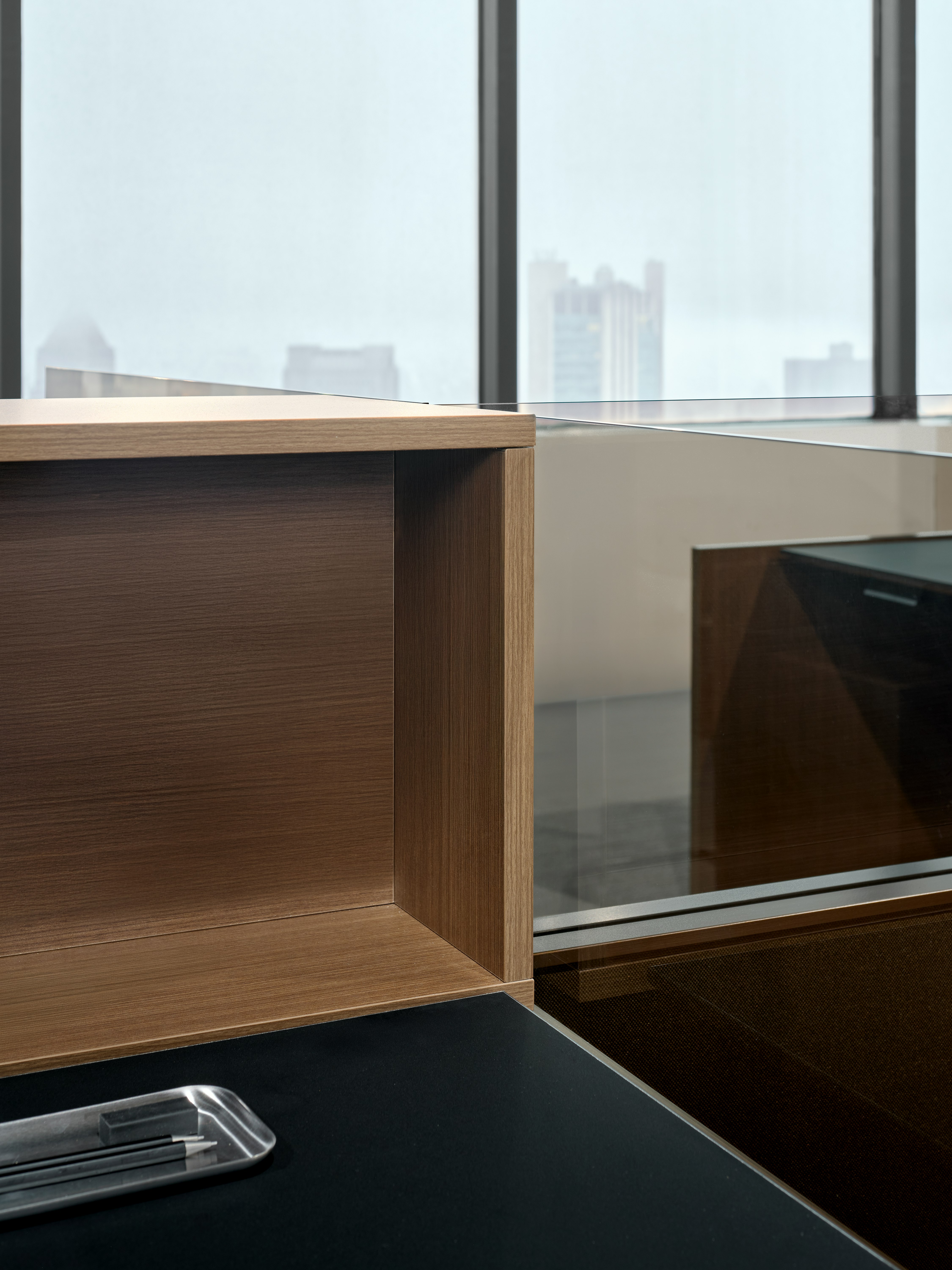 This detail view of a Skyline personal cubby and glass add on is shown at an angle on top of a work surface. There is also a pencil tray sitting on top of the work surface.