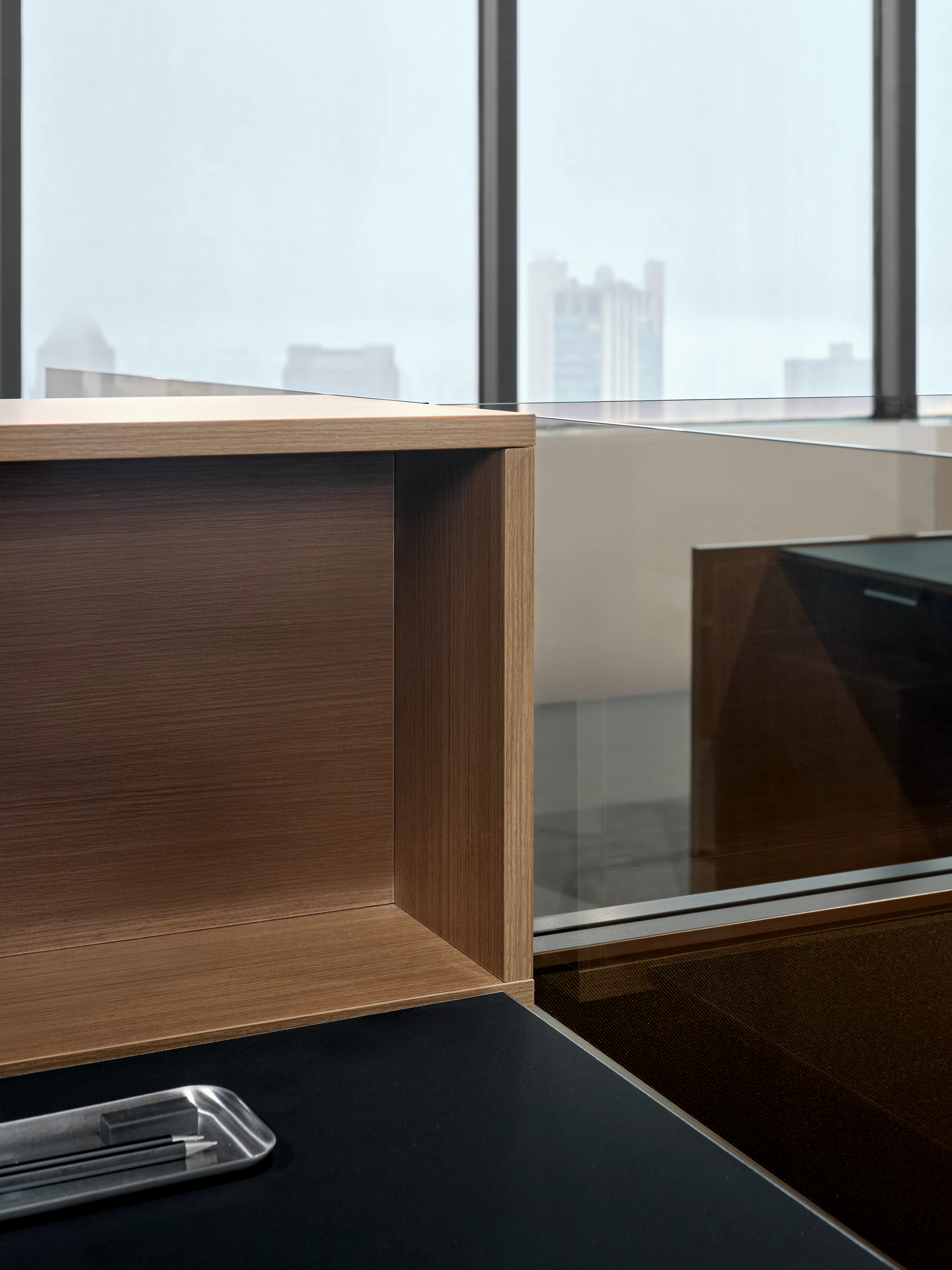 This detail view of a Skyline personal cubby and glass add on is shown at an angle on top of a work surface. There is also a pencil tray sitting on top of the work surface.