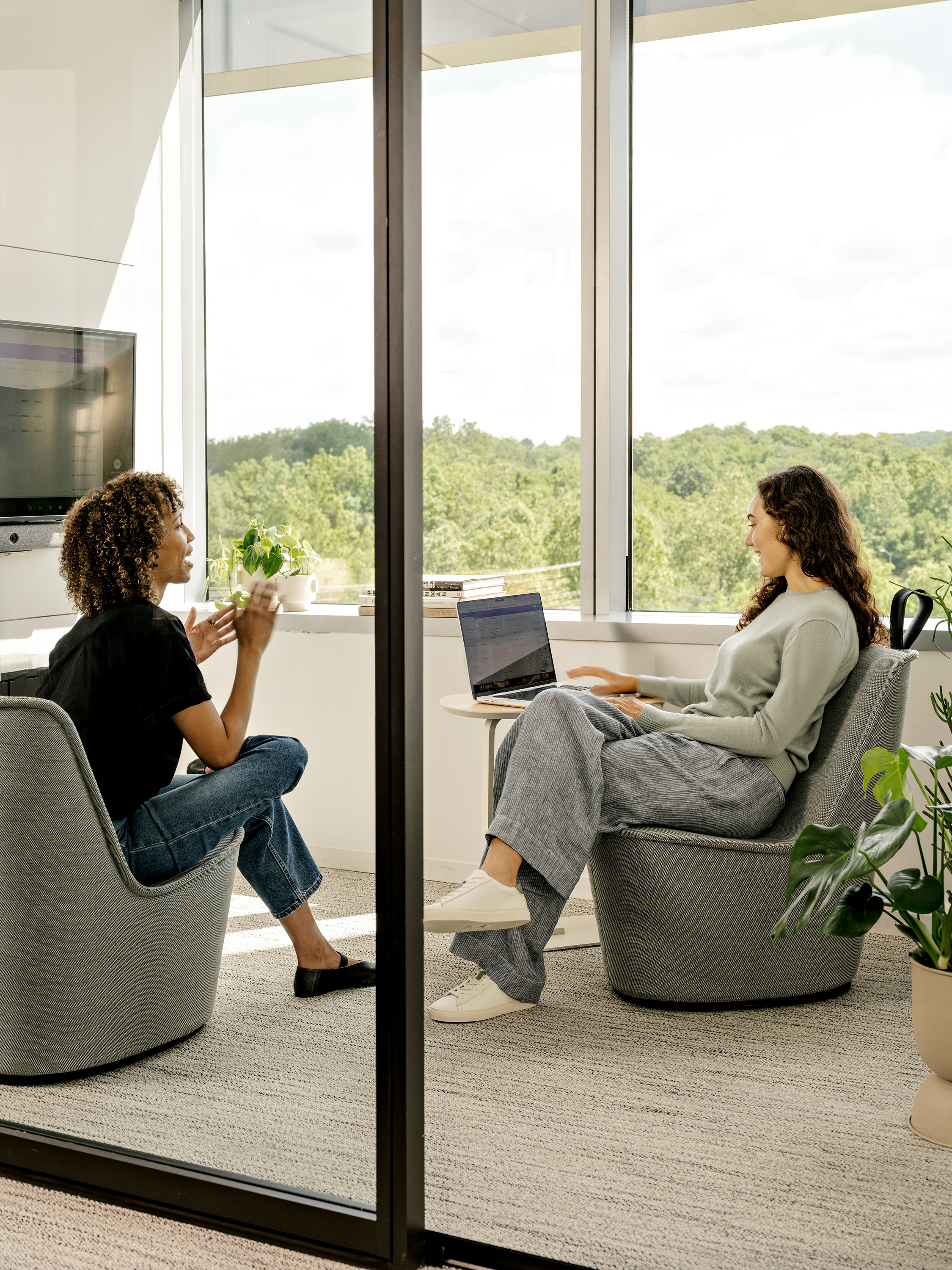 Two women seated in NaughtOne Pippin Chairs having a conversation in a meeting space while one works on her laptop.