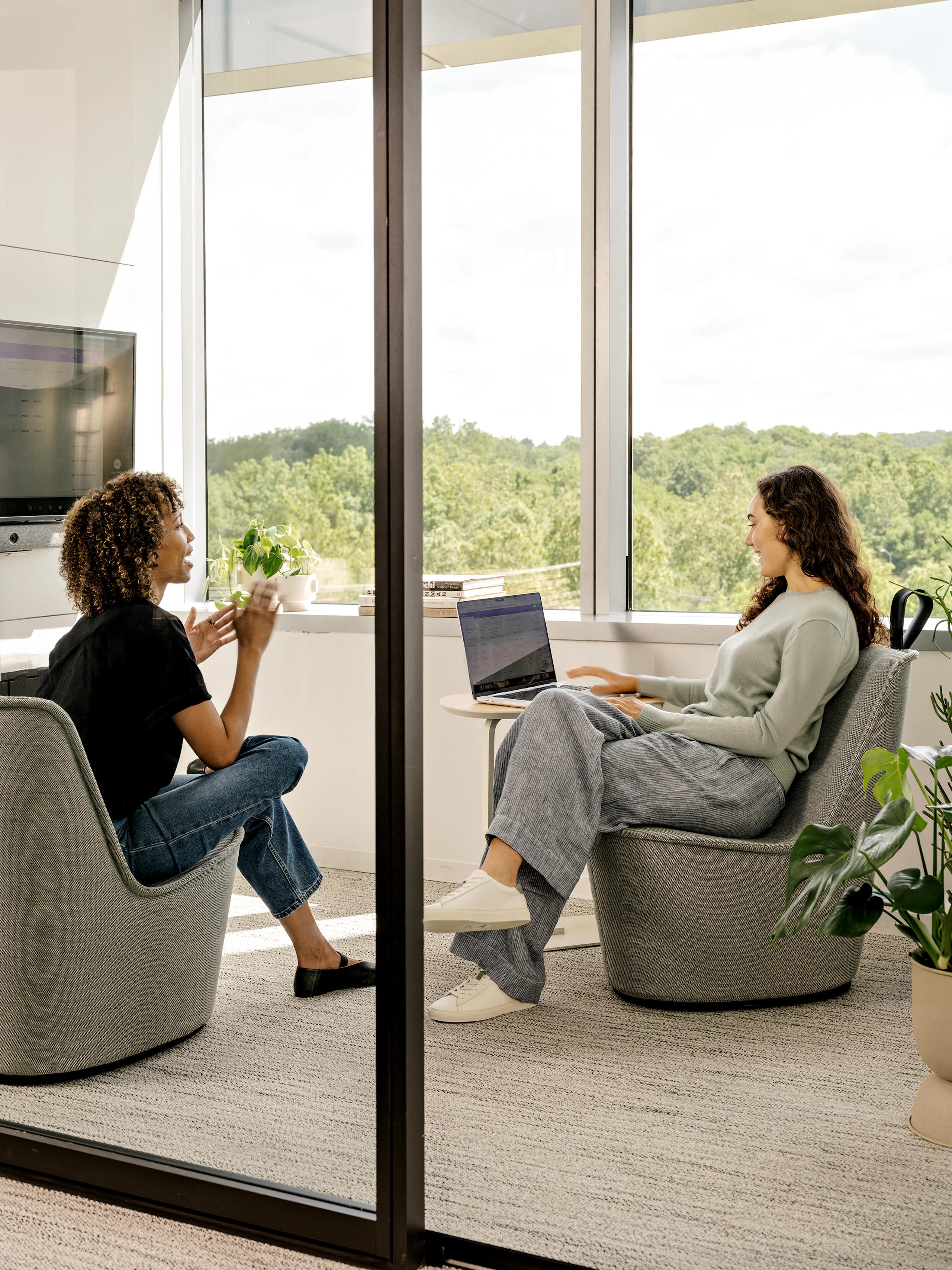 Two women seated in NaughtOne Pippin Chairs having a conversation in a meeting space while one works on her laptop.