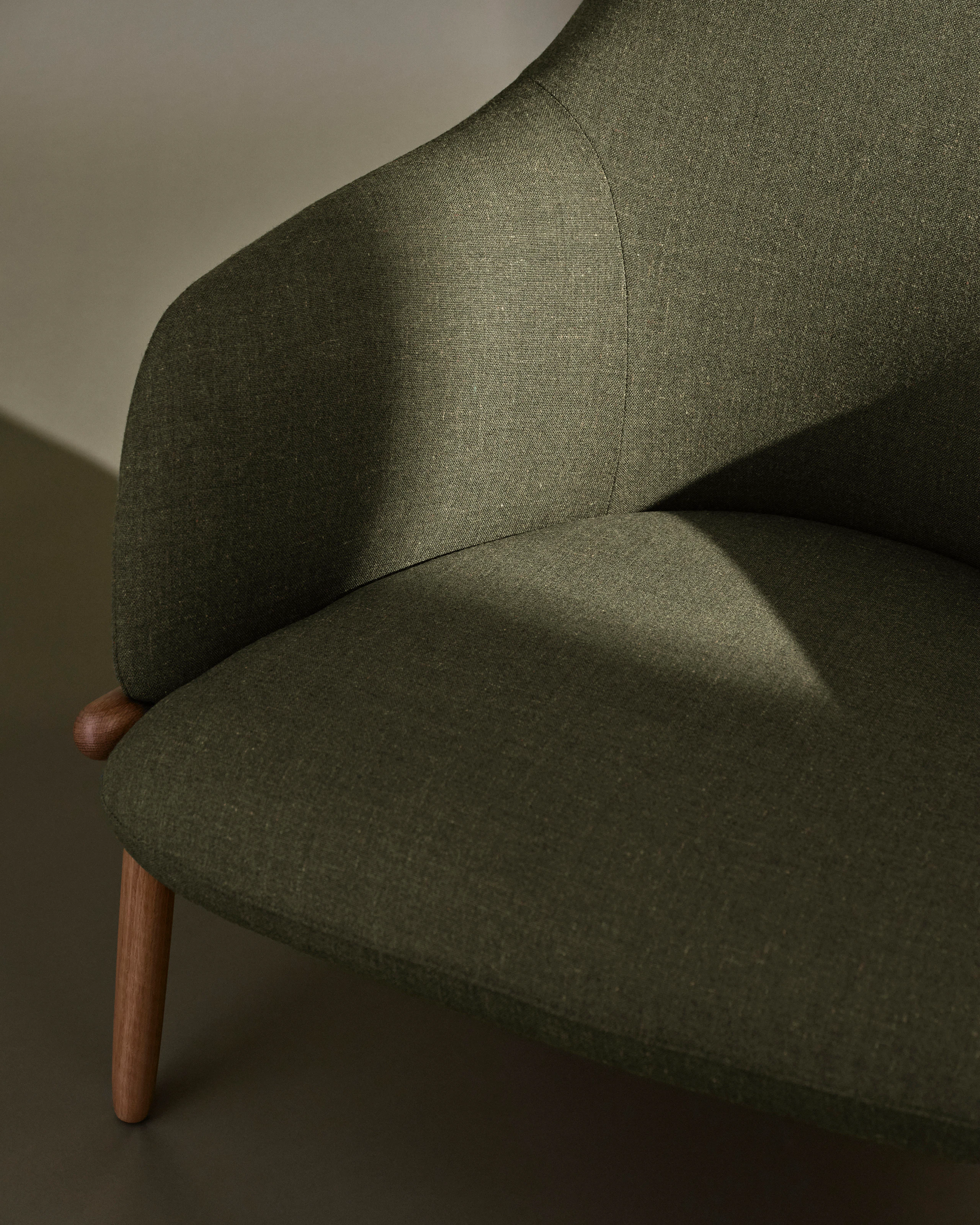 Detail view of a High-Back Reframe Lounge Chair designed by EOOS with an Oak frame upholstered with Rowan in Zucchini, shown at an angle against a neutral studio background.