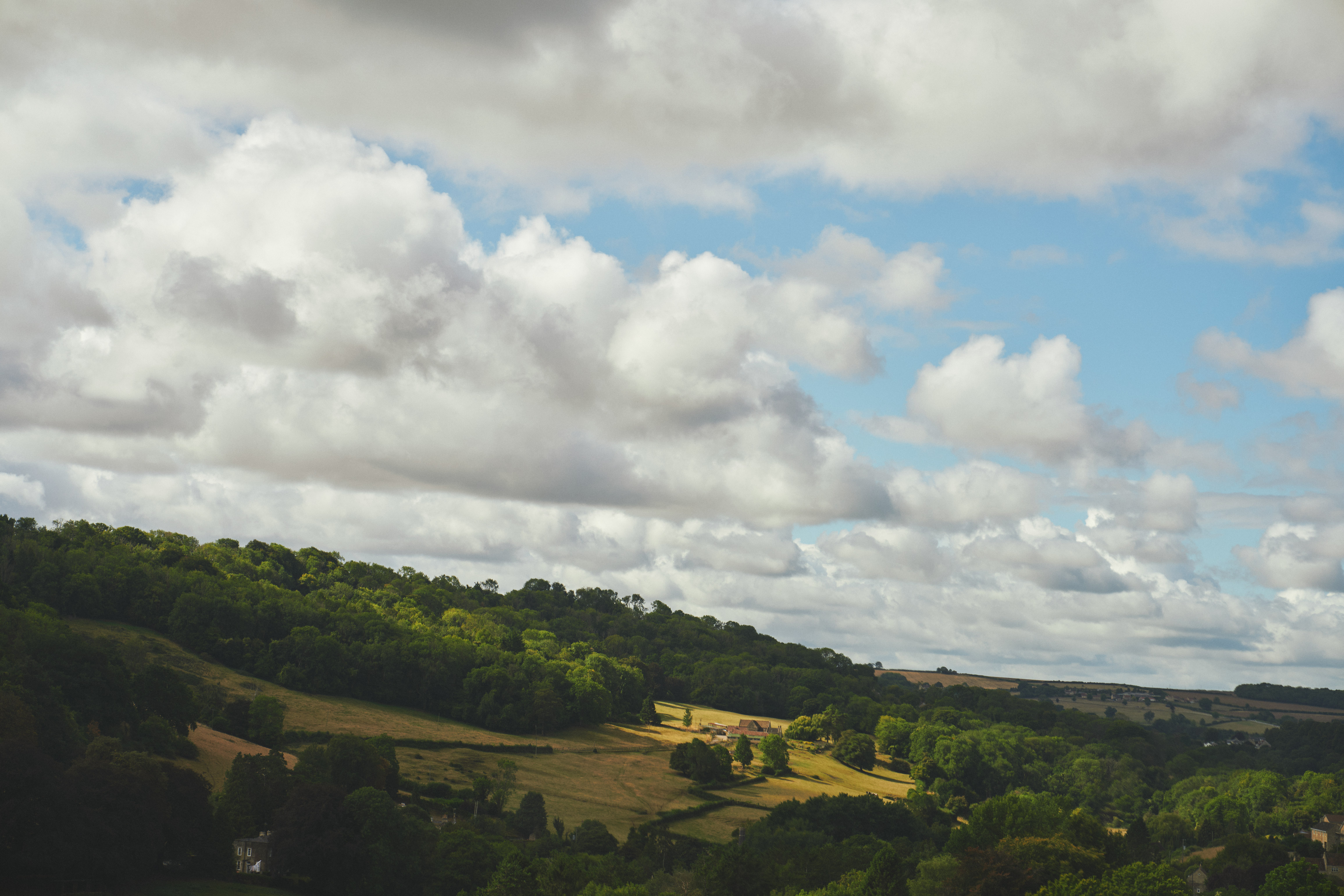   Green, rolling hills blanketed in trees beneath a cloudy sky.