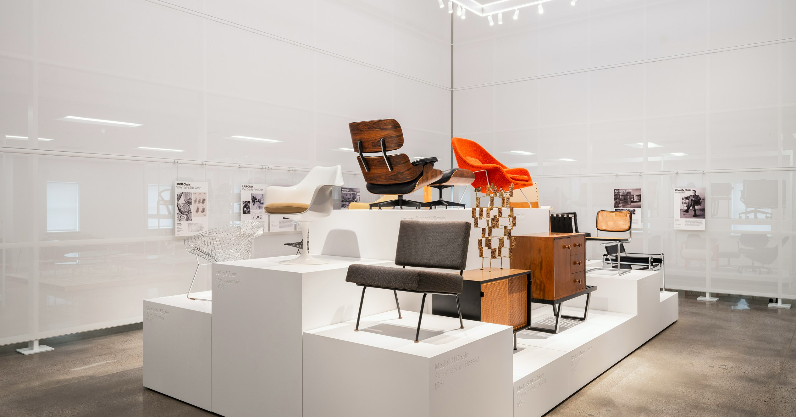 Classic pieces of furniture from the MillerKnoll collective, such as an orange Knoll Womb Chair and black Knoll Barcelona Chair, arranged on white pedestals at the MillerKnoll Archives