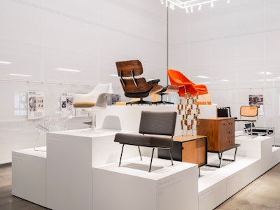 Classic pieces of furniture from the MillerKnoll collective, such as an orange Knoll Womb Chair and black Knoll Barcelona Chair, arranged on white pedestals at the MillerKnoll Archives