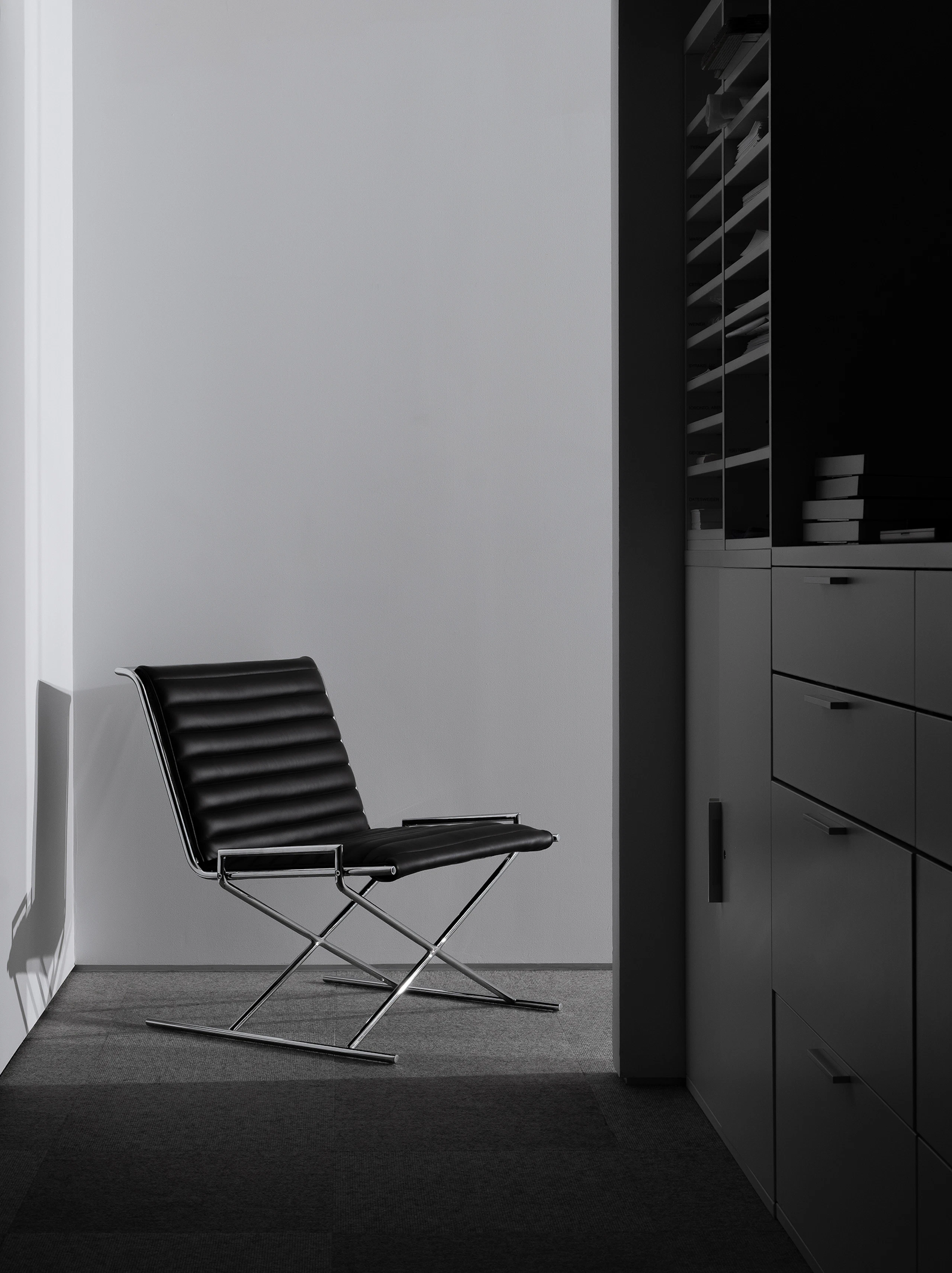 Sled Chair designed by Ward Bennett upholstered with black leather with a chrome frame, viewed in an office setting at an angle.