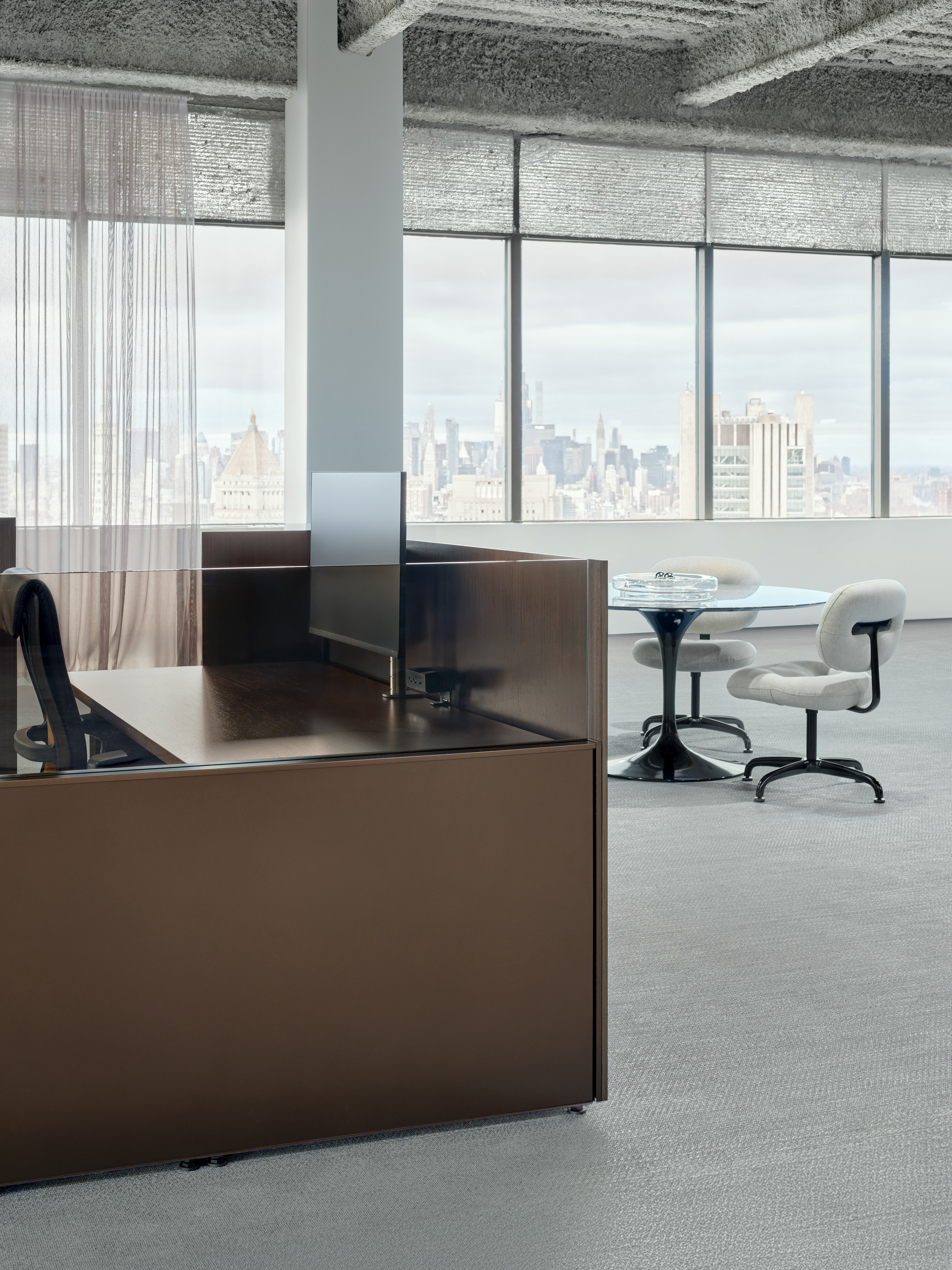 A portion of a work station is viewed at an angle with a meeting table and chairs in the background.