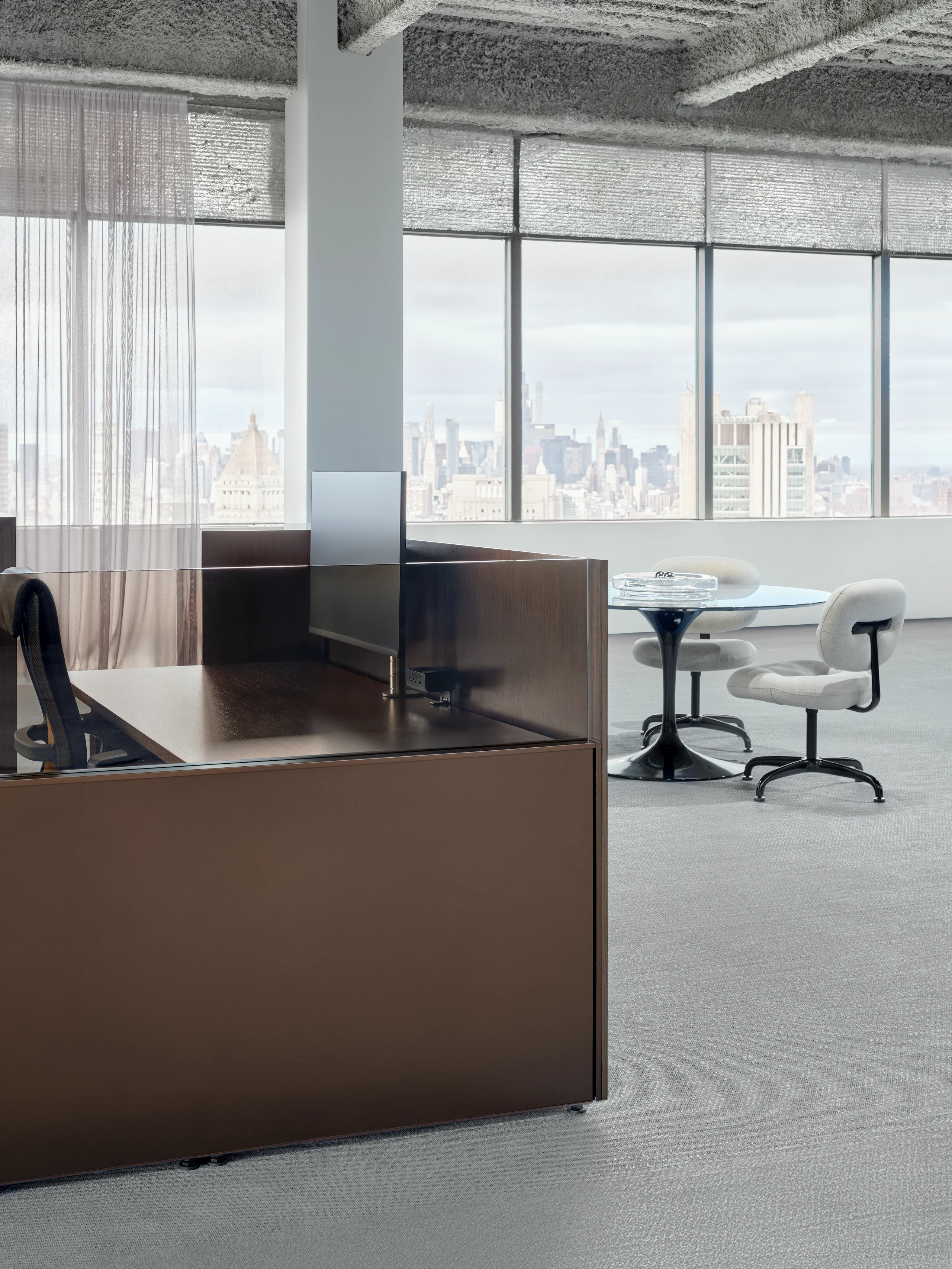 A portion of a work station is viewed at an angle with a meeting table and chairs in the background.