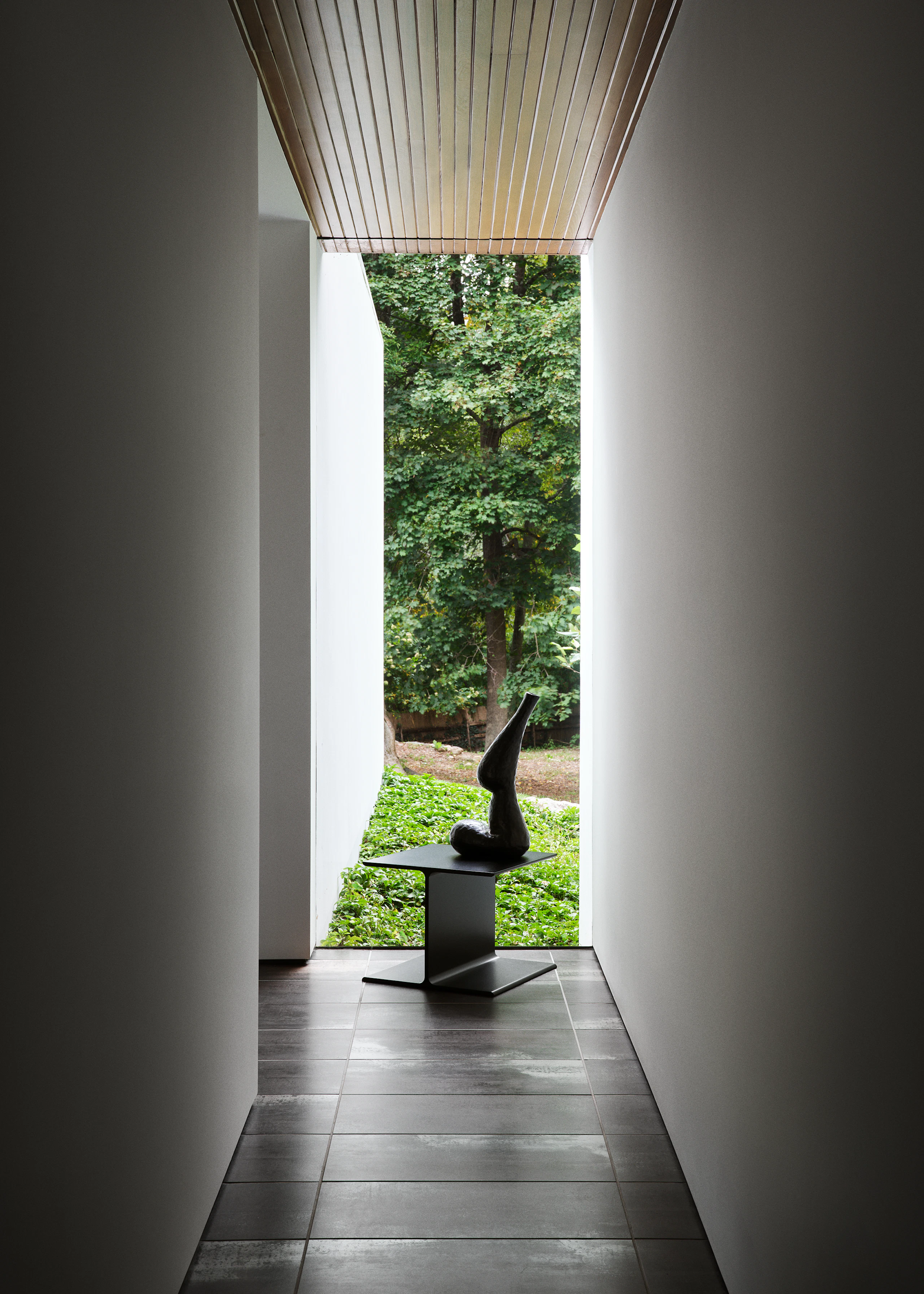I Beam Side Table designed by Ward Bennett in black metal shown in a hallway in front of a window with a sculpture placed on top.