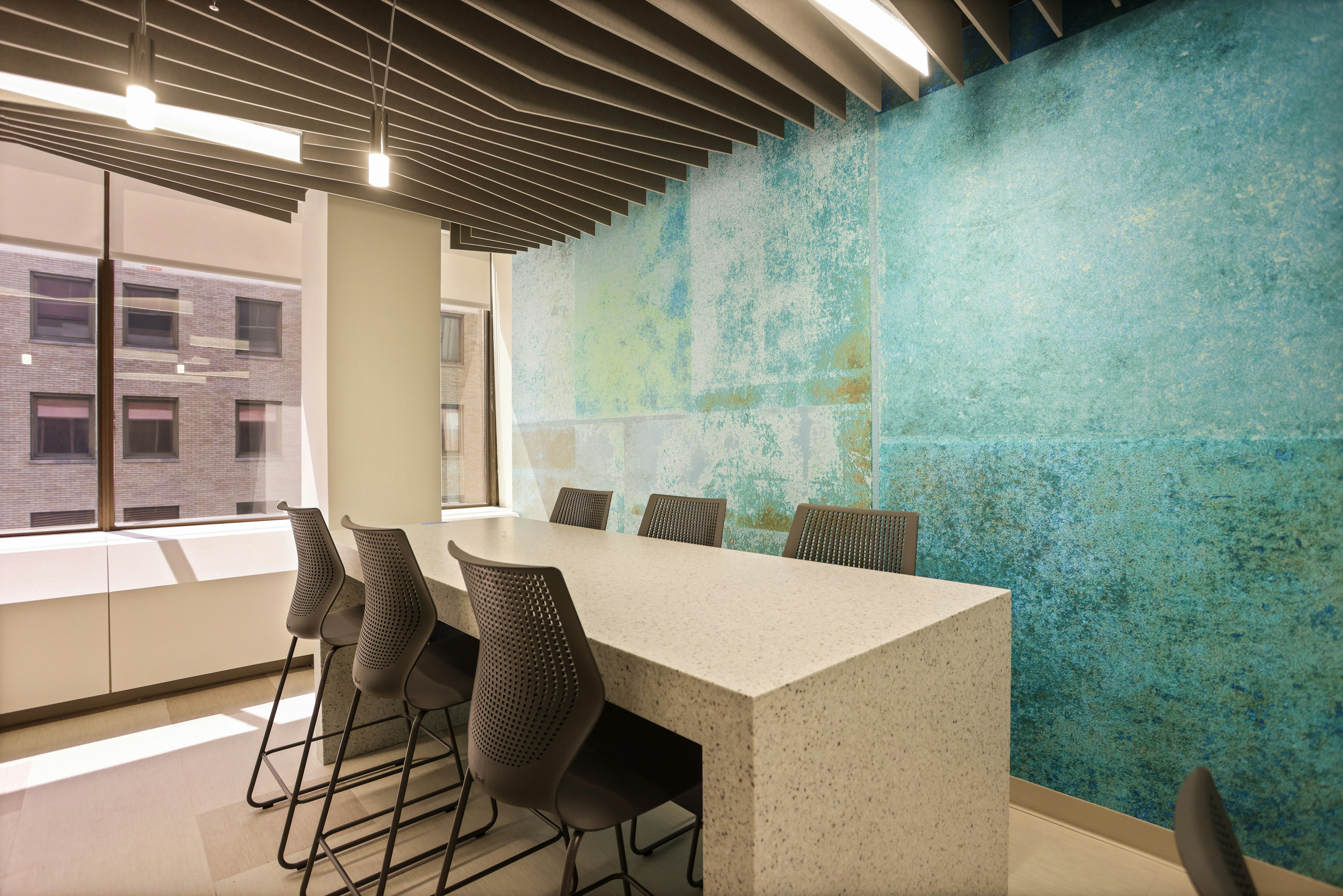 Meeting room furnished with black MultiGeneration by Knoll stools and a bar-height table. One wall is painted a mixture of bright blue and yellow.