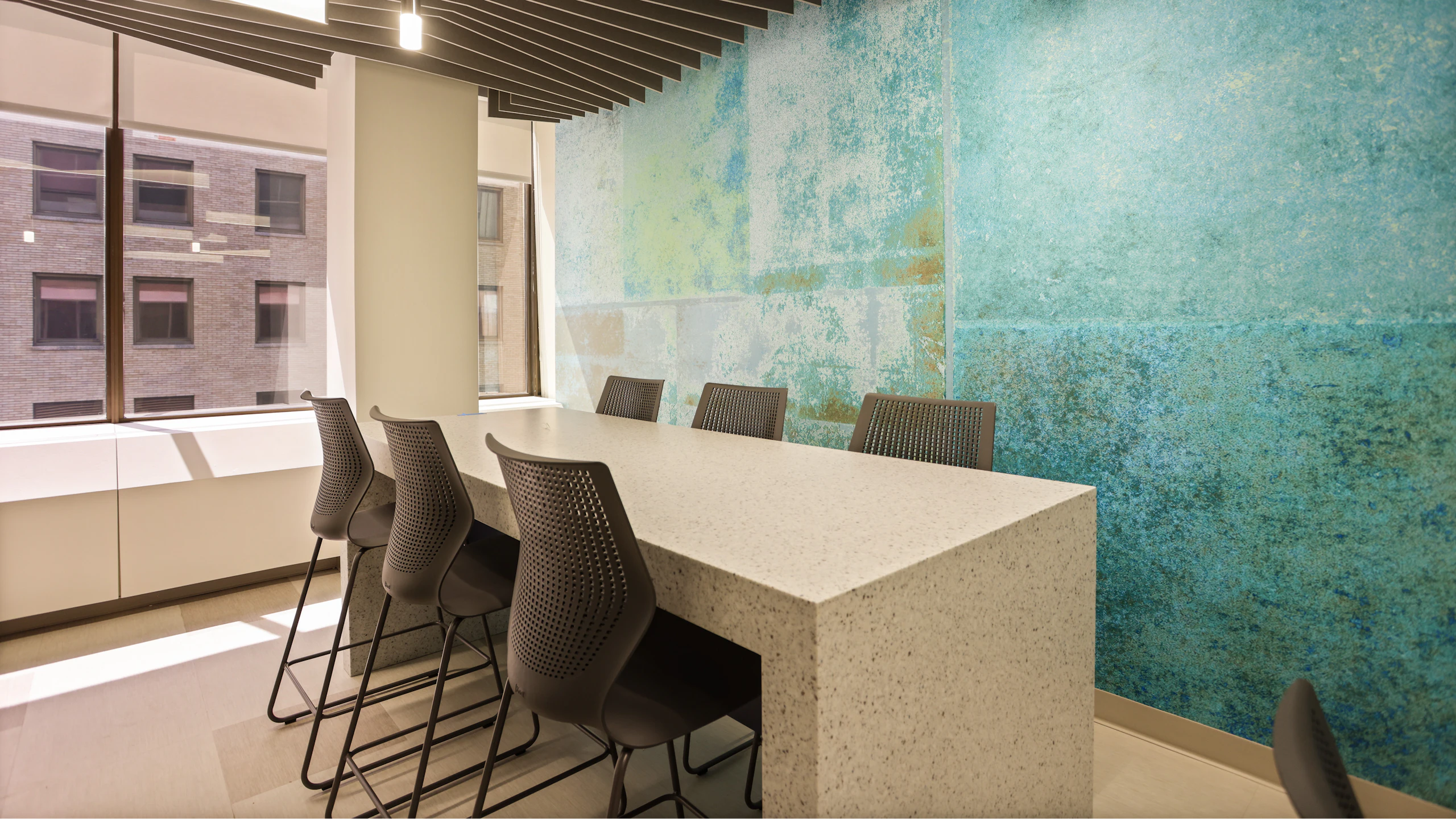 Meeting room furnished with black MultiGeneration by Knoll stools and a bar-height table. One wall is painted a mixture of bright blue and yellow.