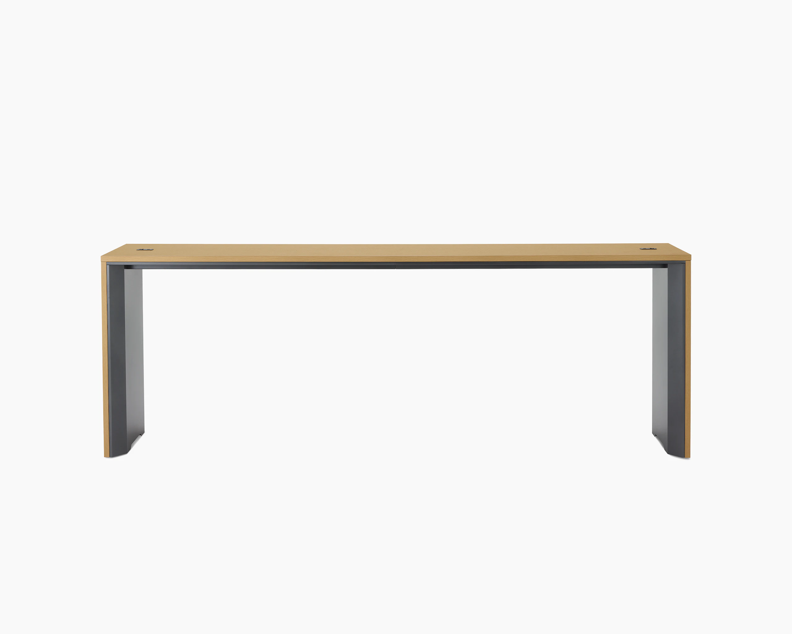 A narrow communal Headway table at standing height with a medium light wood top and dark gray base.