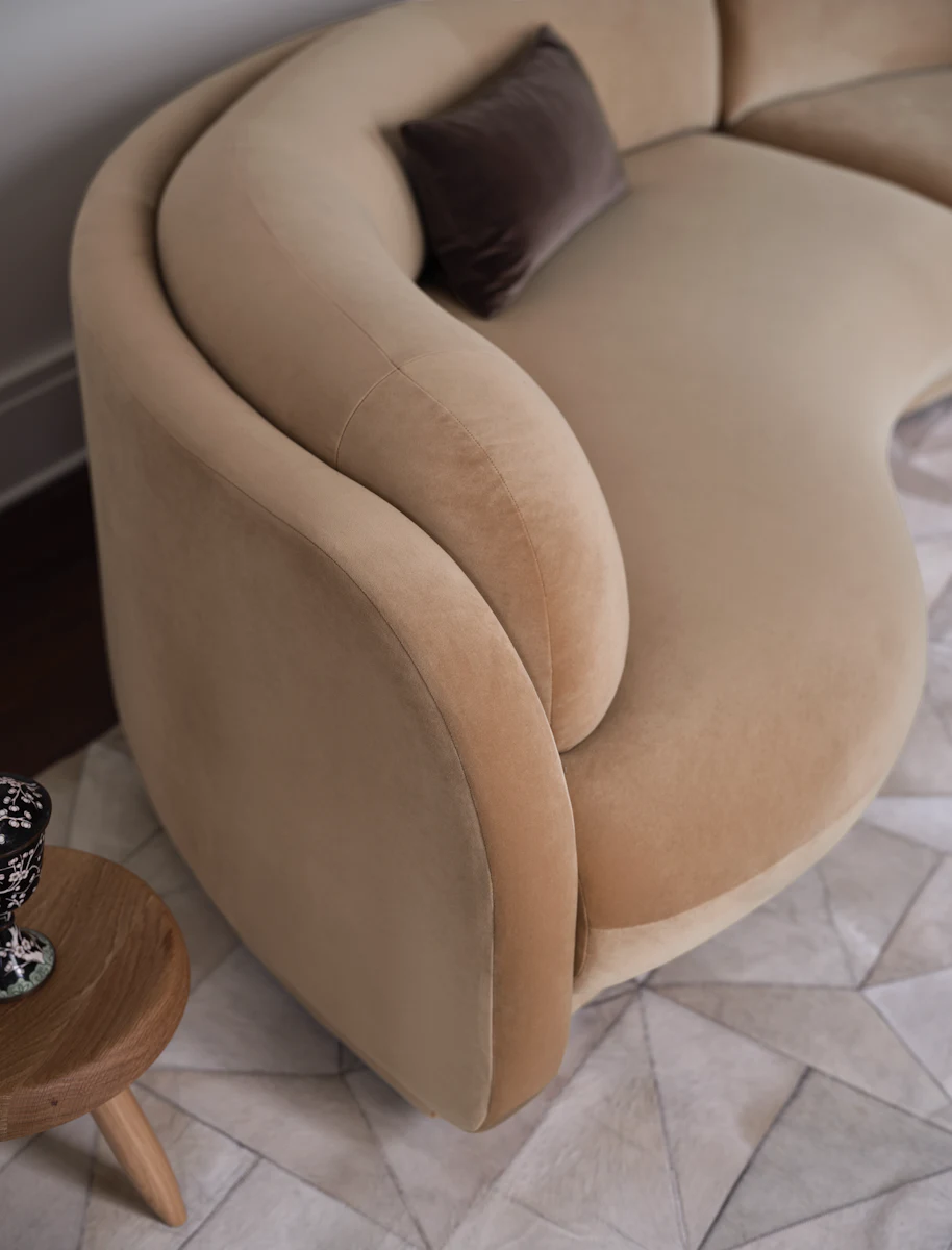 Close-up of beige curved sofa arm and back cushion showing plush fabric