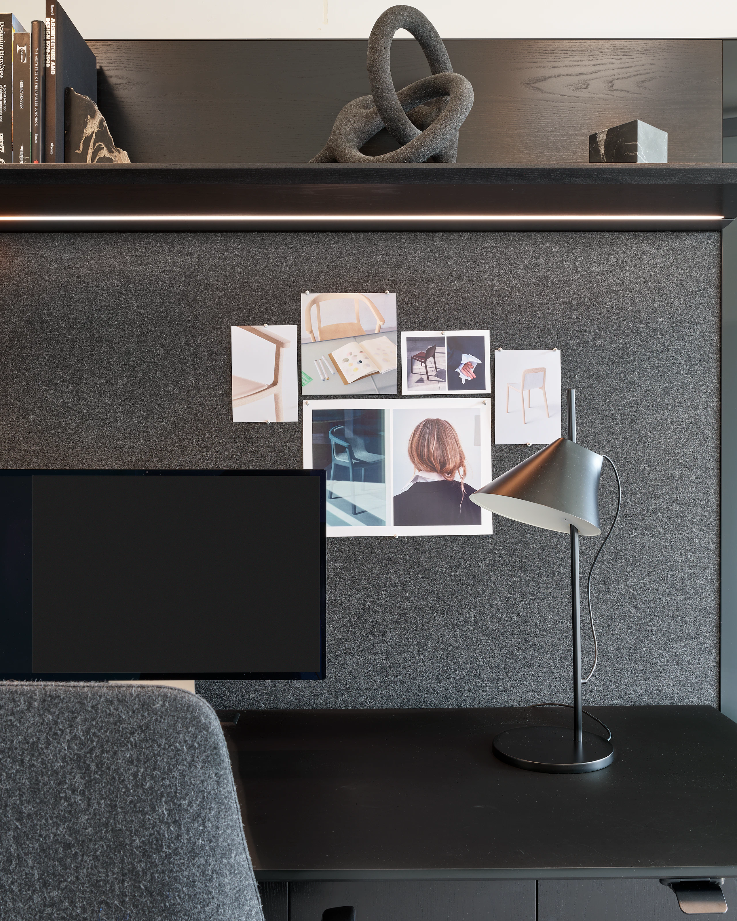 Detail view of a Geiger One Casegoods work surface, tackboard, and overhead shelving with integrated lighting in Ebonized Flat Cut Ash and a grey textile, viewed from the front in a private office setting.