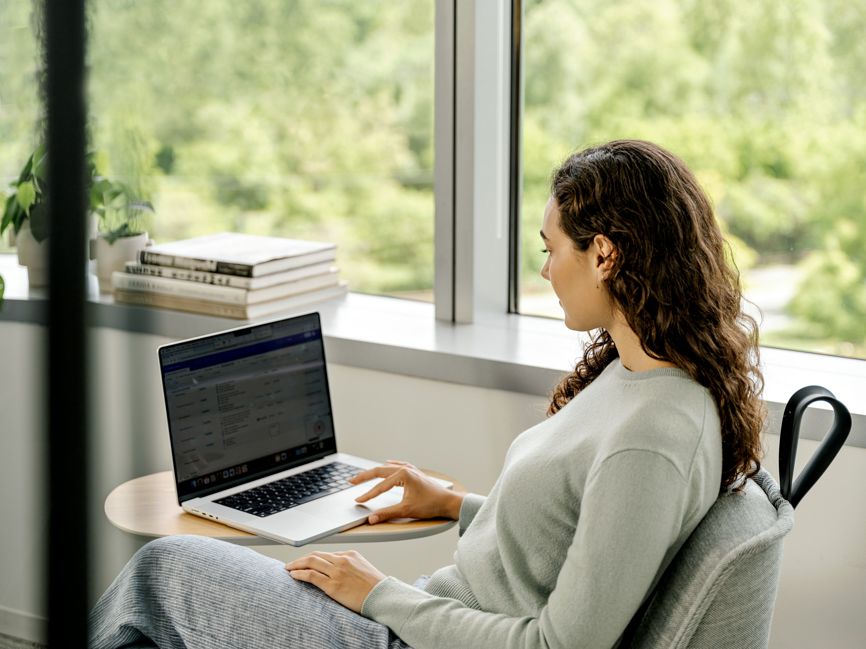 A woman sitting in a chair while working on a laptop at a Herman Miller Passport table.