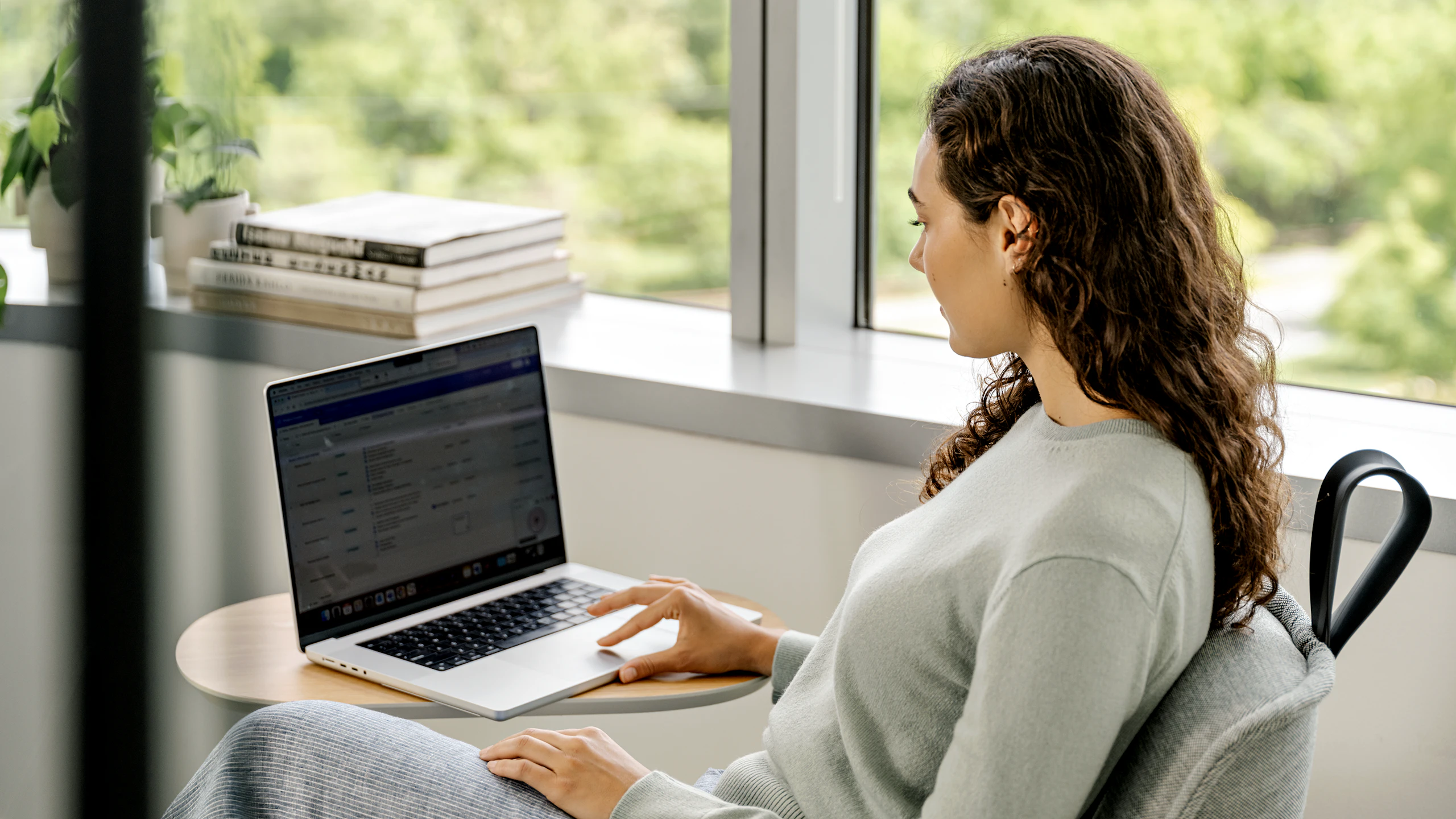 A woman sitting in a chair while working on a laptop at a Herman Miller Passport table.