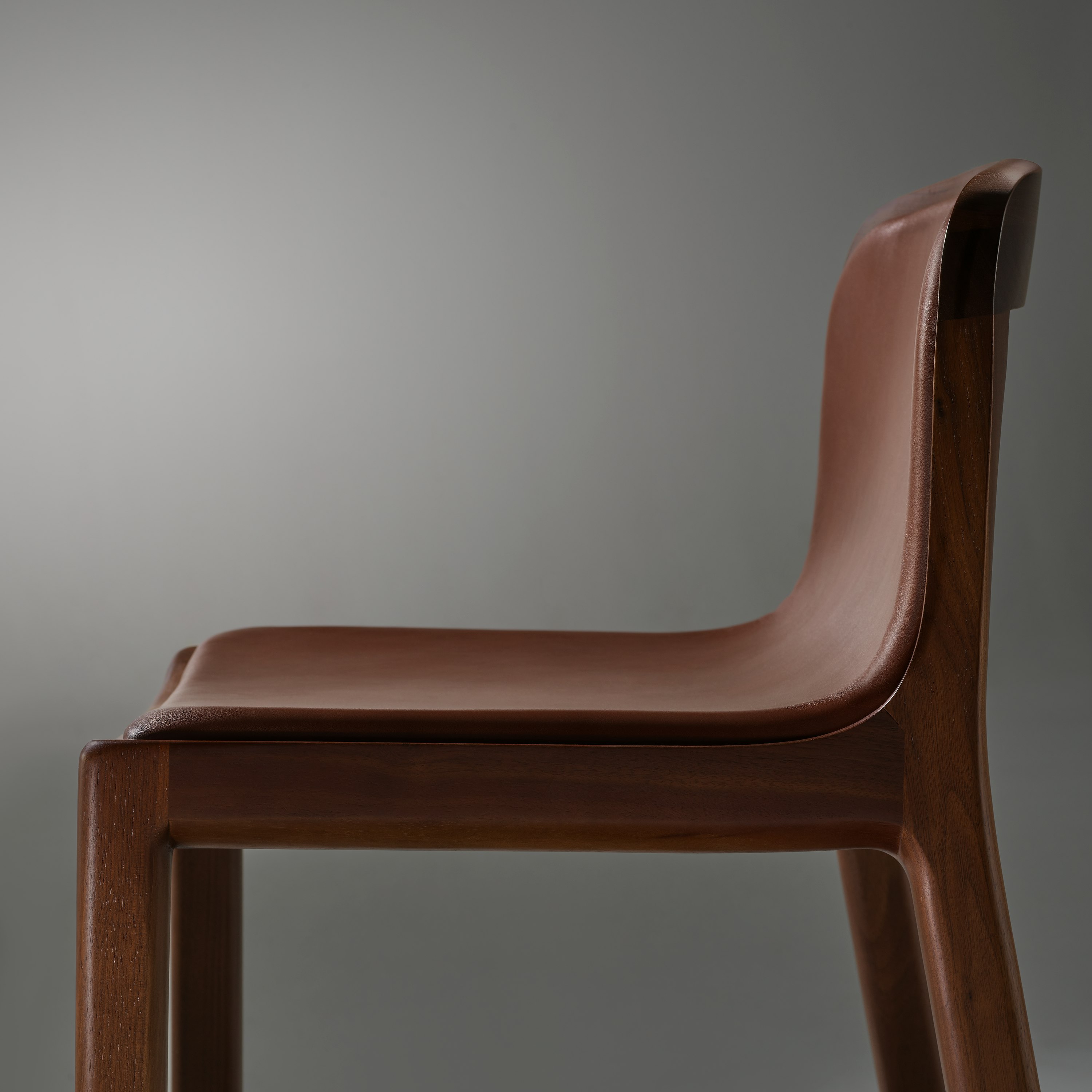 Lijn Stool by Carole Baijings for Geiger in Persian Walnut frame upholstered with Maharam Hue Leather in Bittersweet, detail shot on a grey background.
