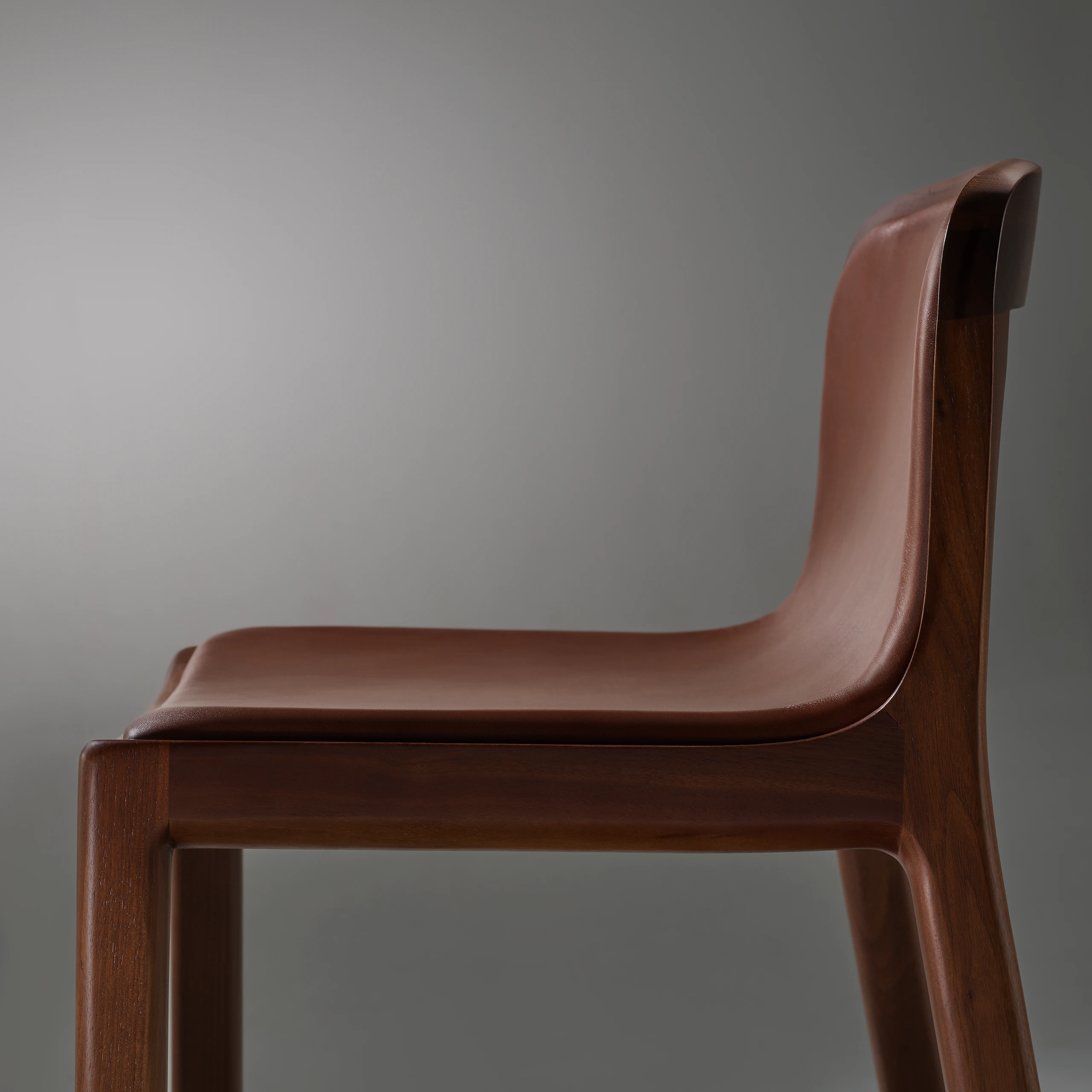 Lijn Stool by Carole Baijings for Geiger in Persian Walnut frame upholstered with Maharam Hue Leather in Bittersweet, detail shot on a grey background.