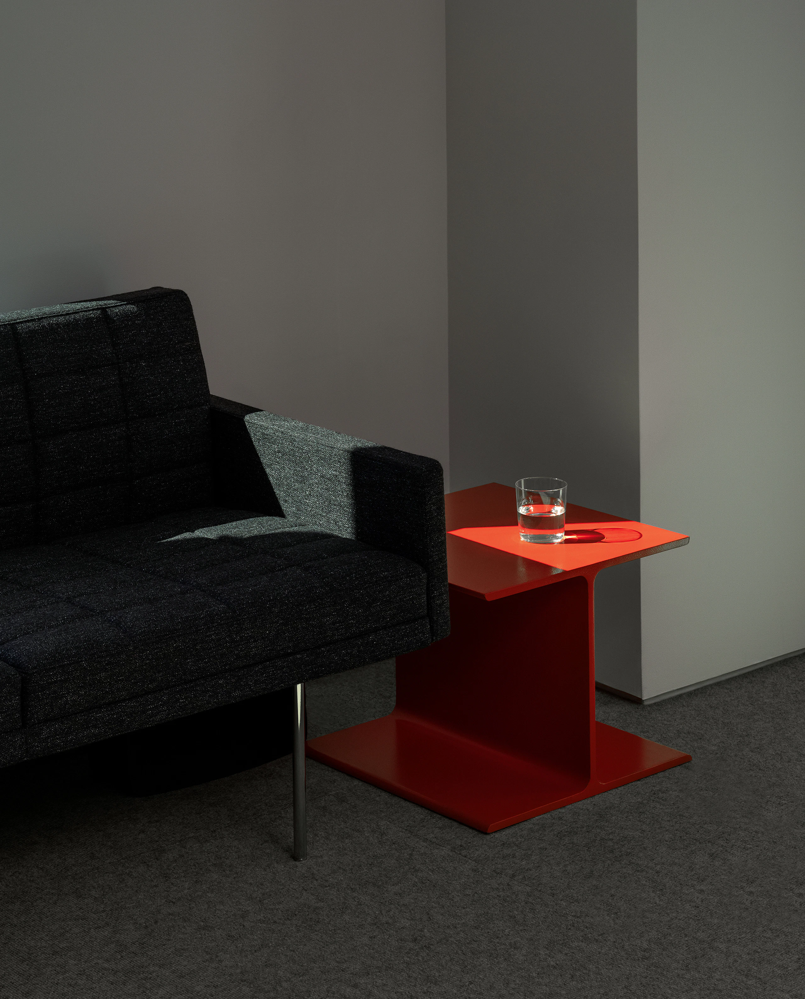 Tuxedo Component Sofa upholstered with Bellano textile in Black Green beside an orange I Beam Side Table in a showroom setting, at an angle.
