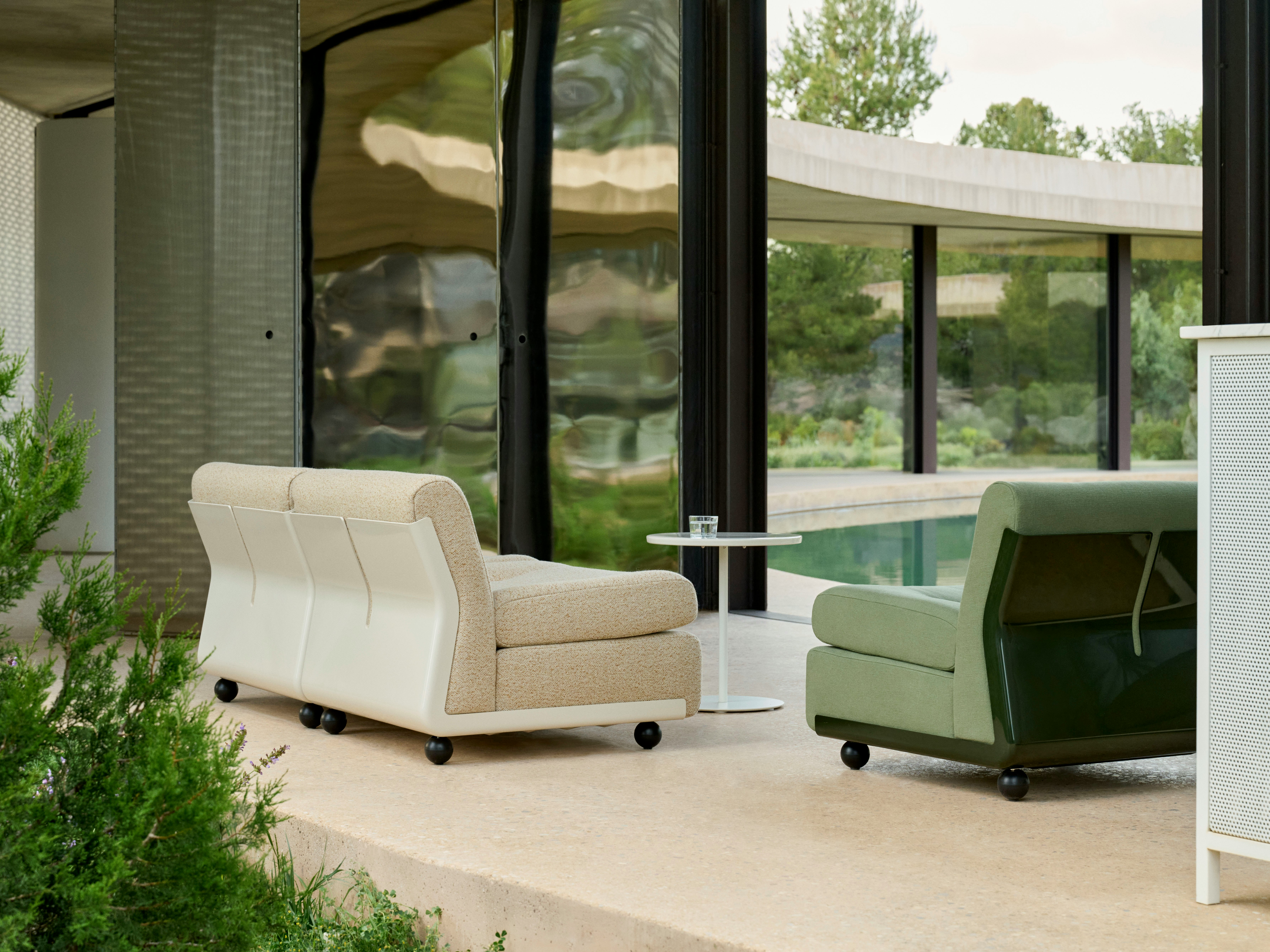 Two Amanta lounge chairs—one beige, one green—on a patio outside a midcentury-style home.