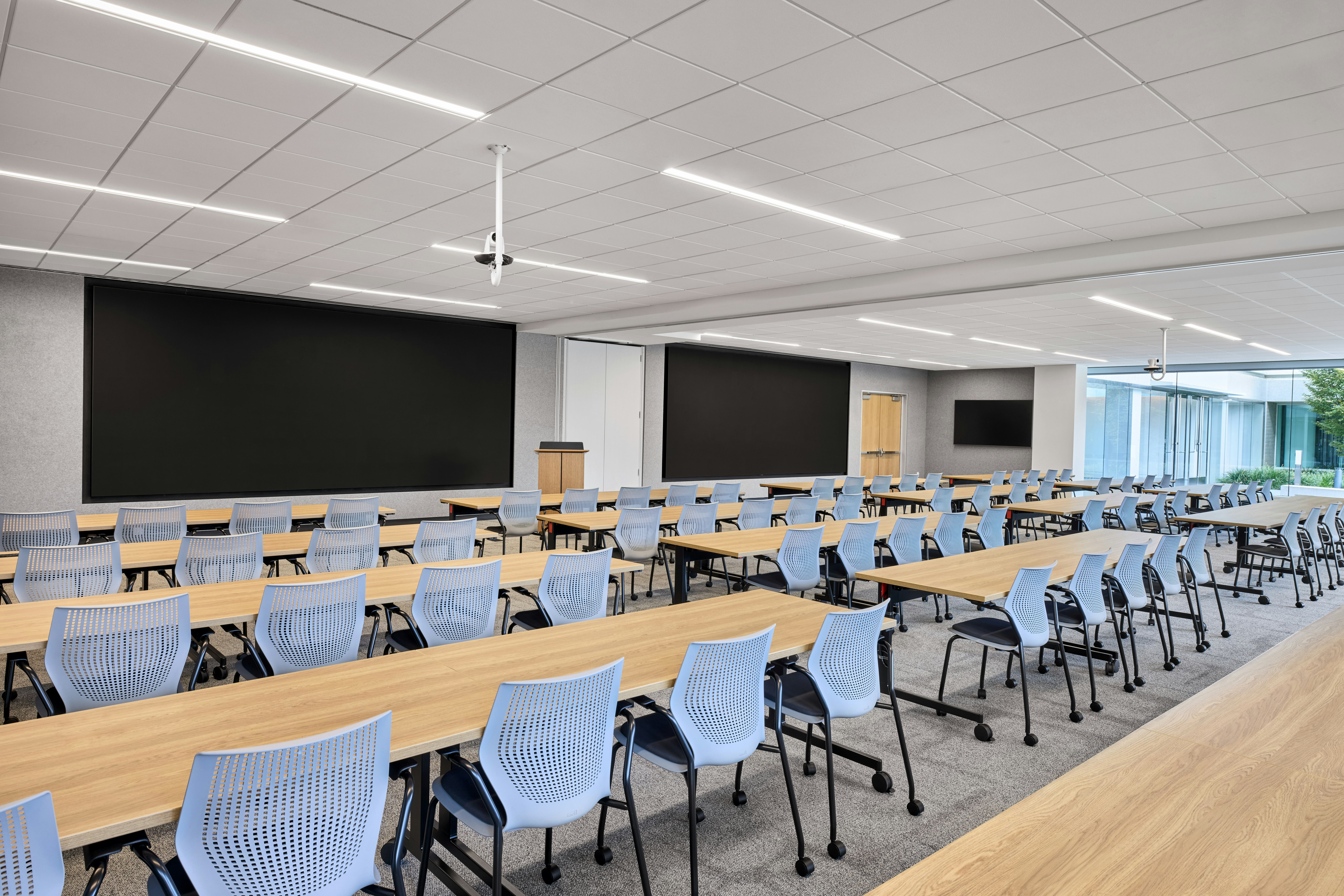 Classroom environment featuring mobile tables arranged in rows with MultiGeneration by Knoll stacking chairs, and a large presentation board.