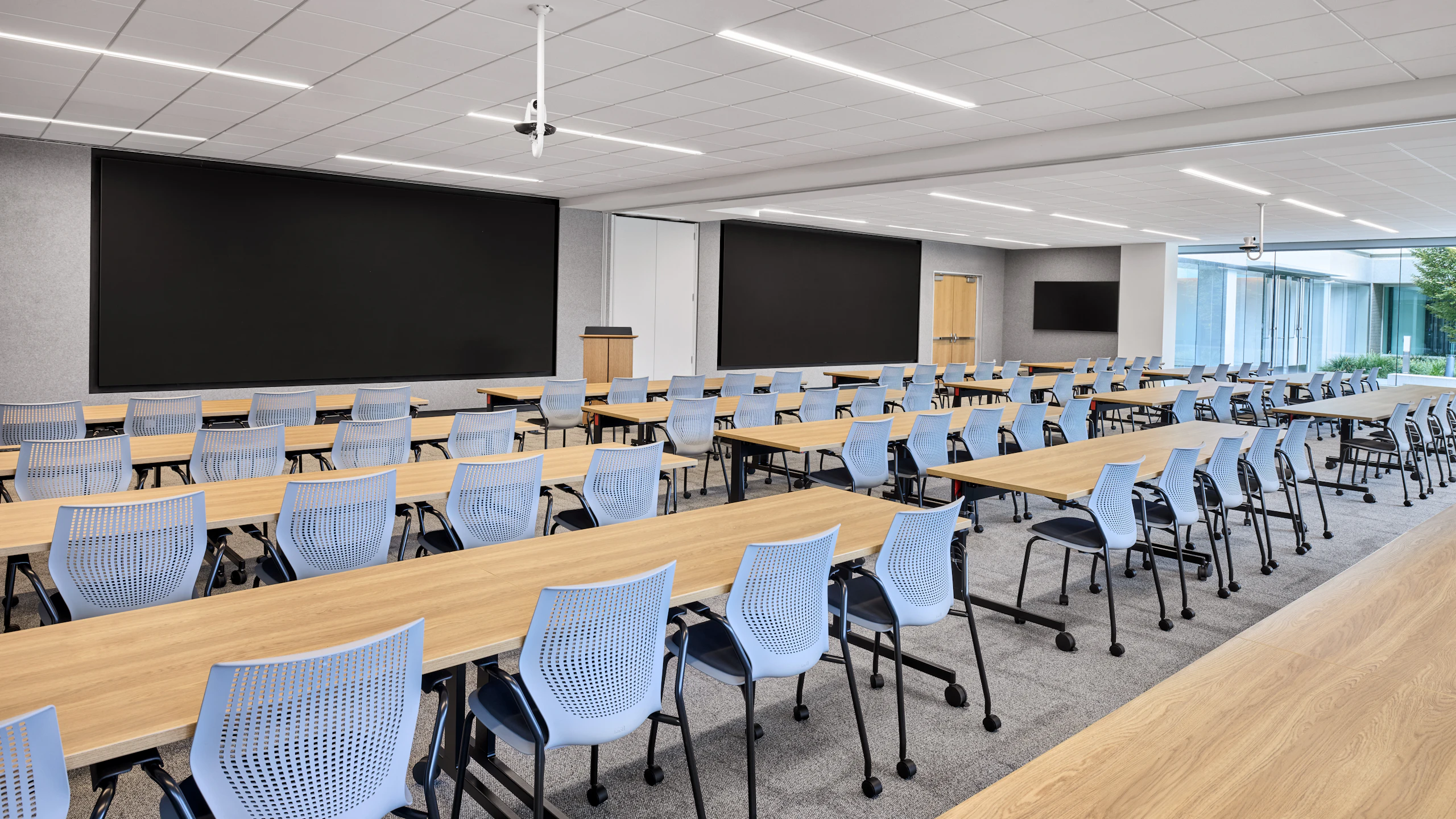 Classroom environment featuring mobile tables arranged in rows with MultiGeneration by Knoll stacking chairs, and a large presentation board.