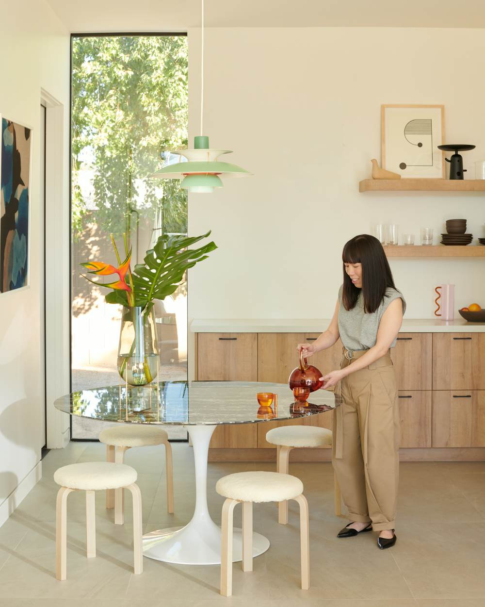 Christine Lin with Saarinen Dining Table,  Maharam Edition Artek Aalto Stool 60,  PH5 Pendant Lamp,  Echasse Vase,  Paola C Teapot and Teacups,  Nelson Star Clock,  Wave Pitcher,  Reaction Poetique Centerpiece