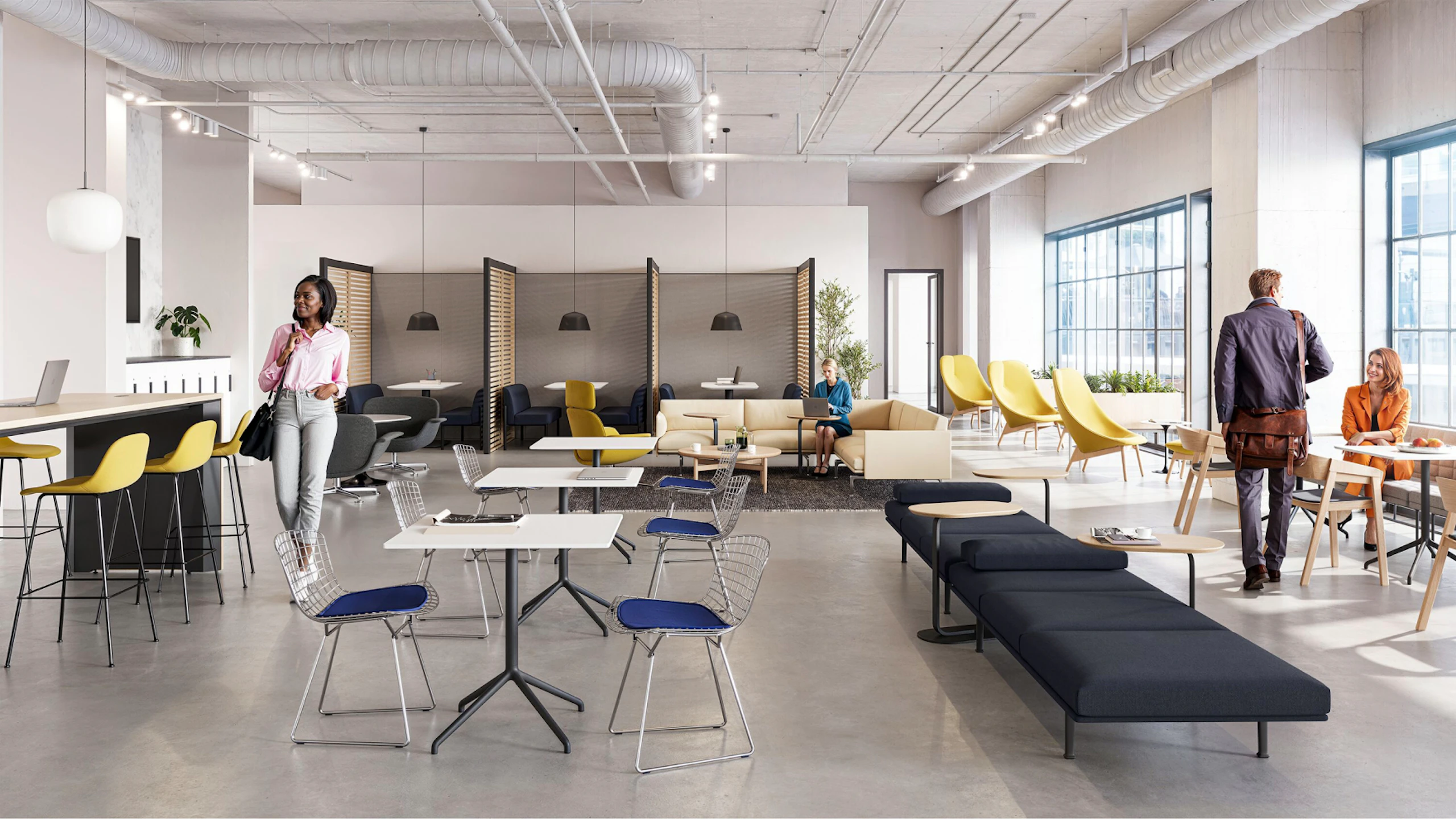 A brightly lit community setting featuring four persons utilizing a variety of colorful seating options including the HAY Uchiwa Lounge Chair, Muuto Base Tables, and Muuto Still Cafe Tables
