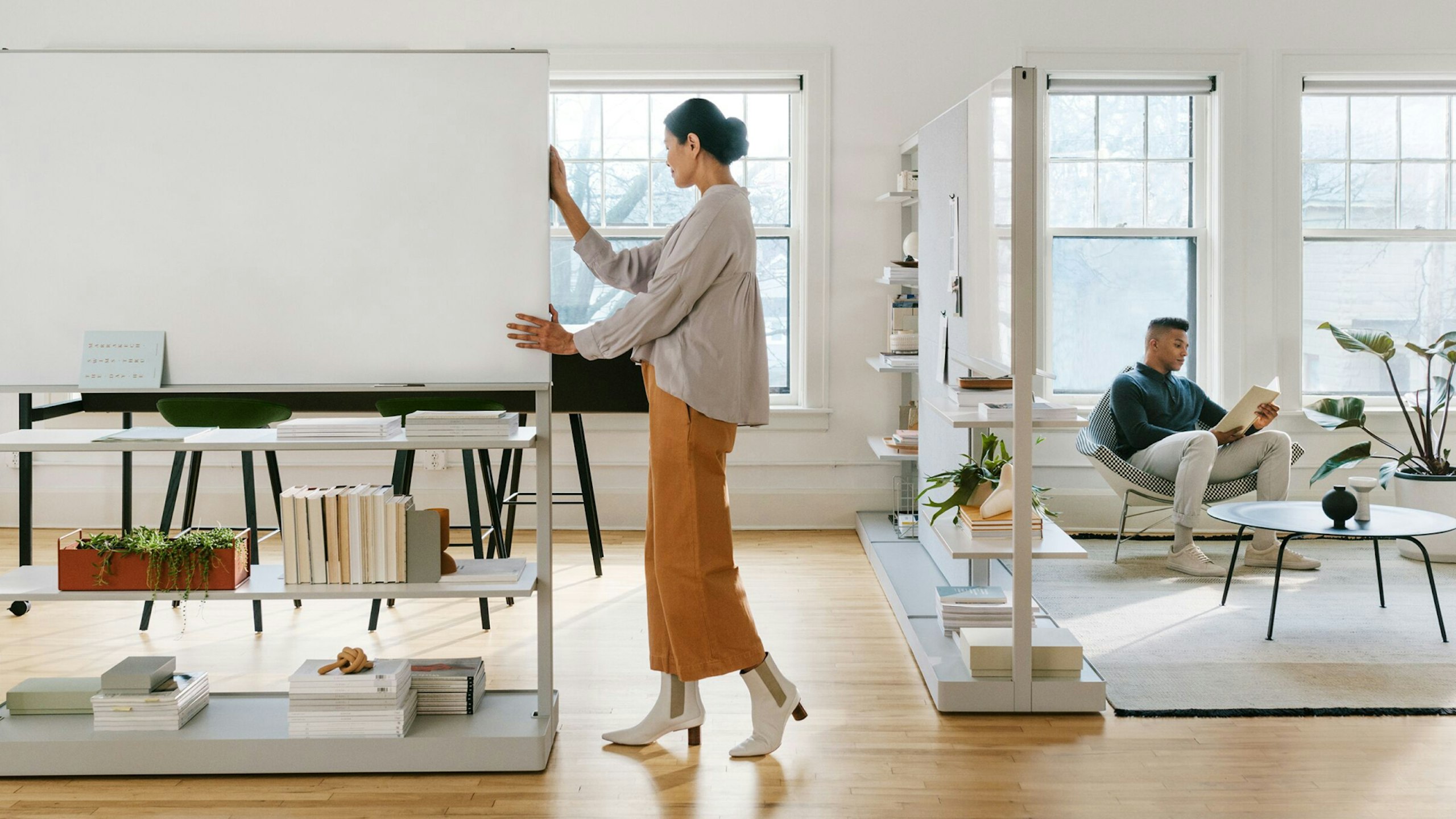 A woman moving a gray OE1 Agile Wall with a man sitting on a checkerboard Nelson Coconut Lounge Chair in the background.