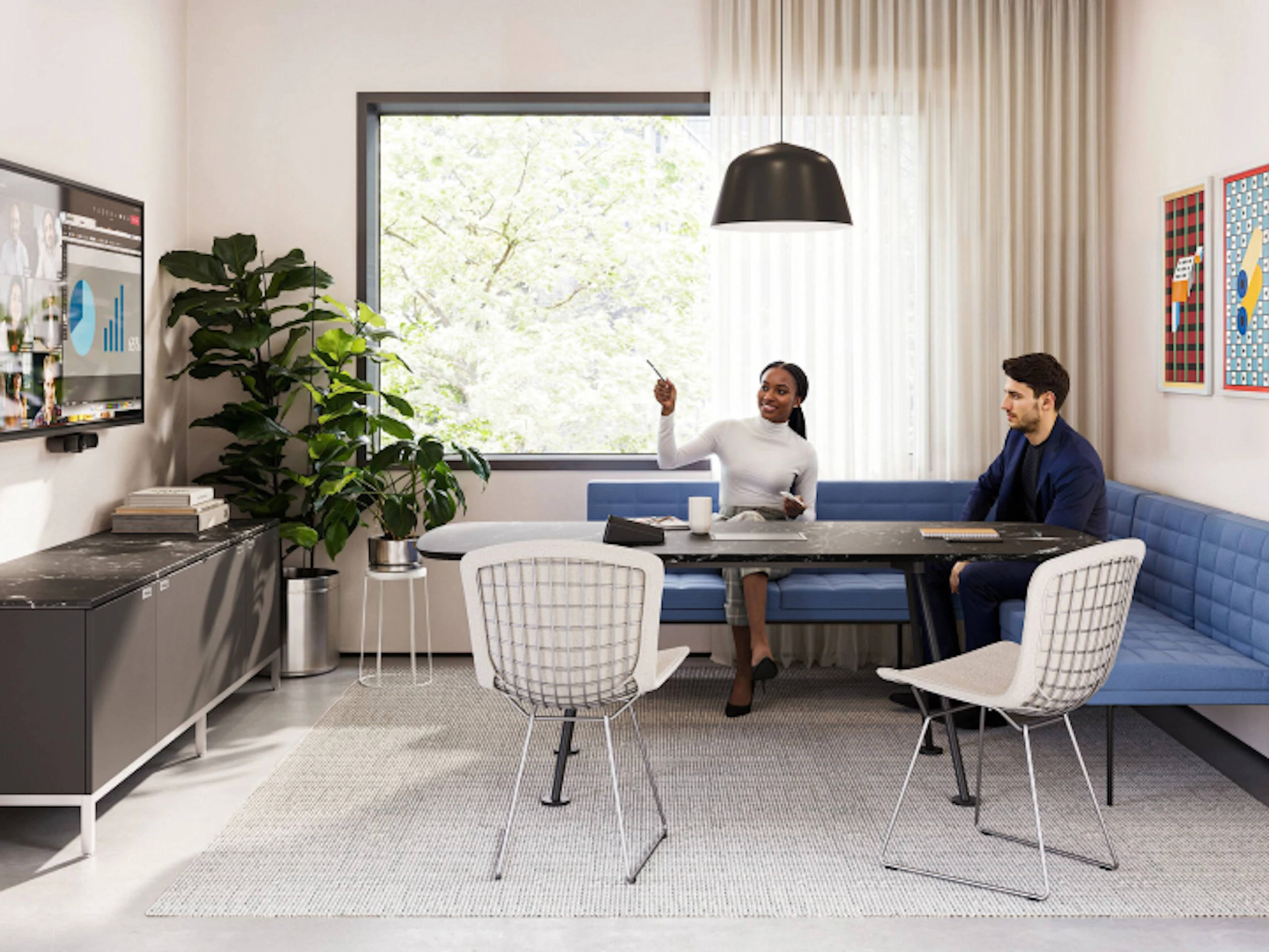 A group setting featuring two people sitting on a blue corner bench while participating in a virtual meeting in a conference room furnished with Geiger Tuxedo Component lounge seating, a Knoll Grasshopper Table and a Knoll Florence Knoll Credenza