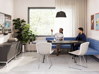 A group setting featuring two people sitting on a blue corner bench while participating in a virtual meeting in a conference room furnished with Geiger Tuxedo Component lounge seating, a Knoll Grasshopper Table and a Knoll Florence Knoll Credenza