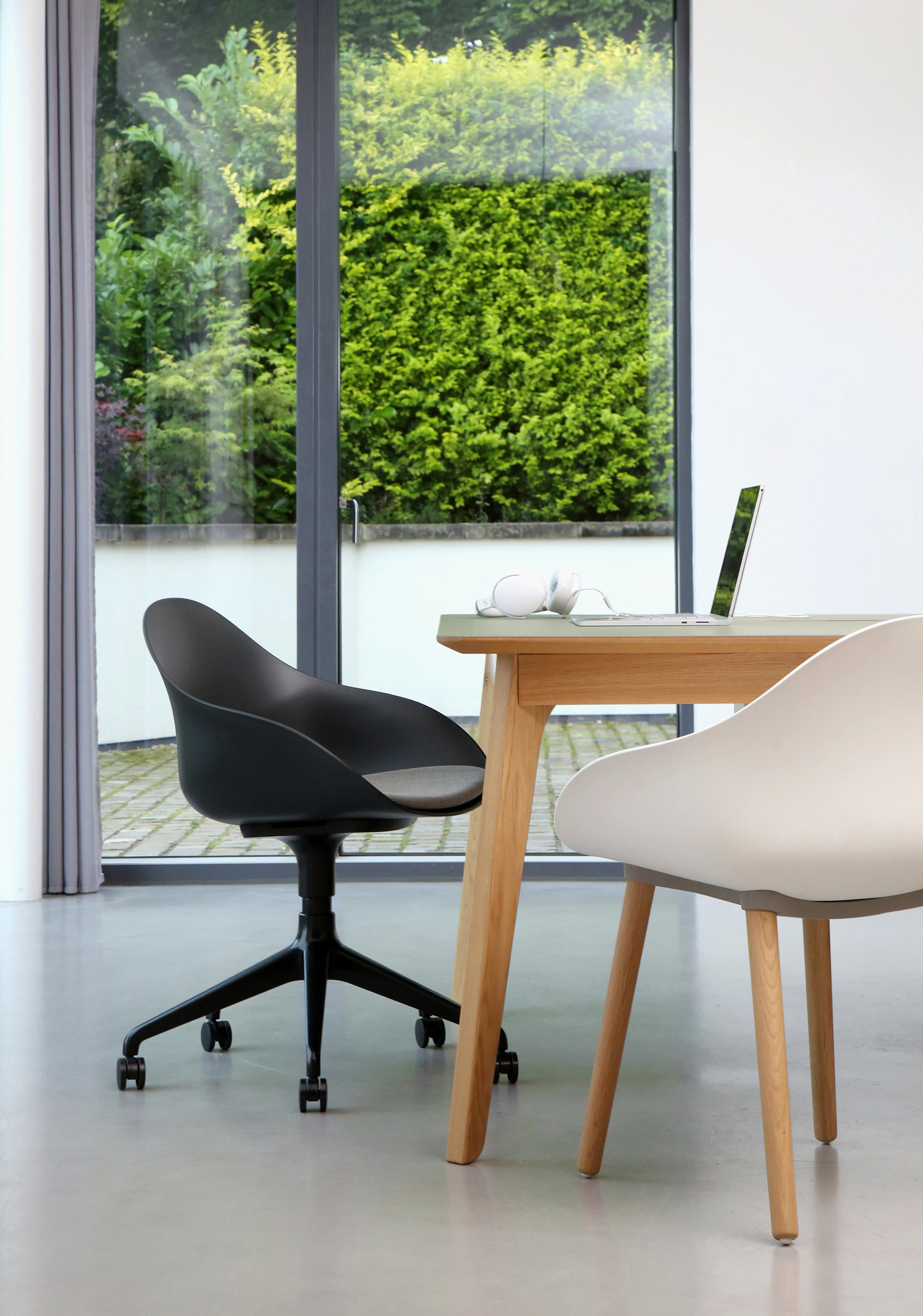 A black Ruby Chair with matching 5-star base with grey seat pad and casters is next to a white Ruby side chair on oak dowel base and a table.